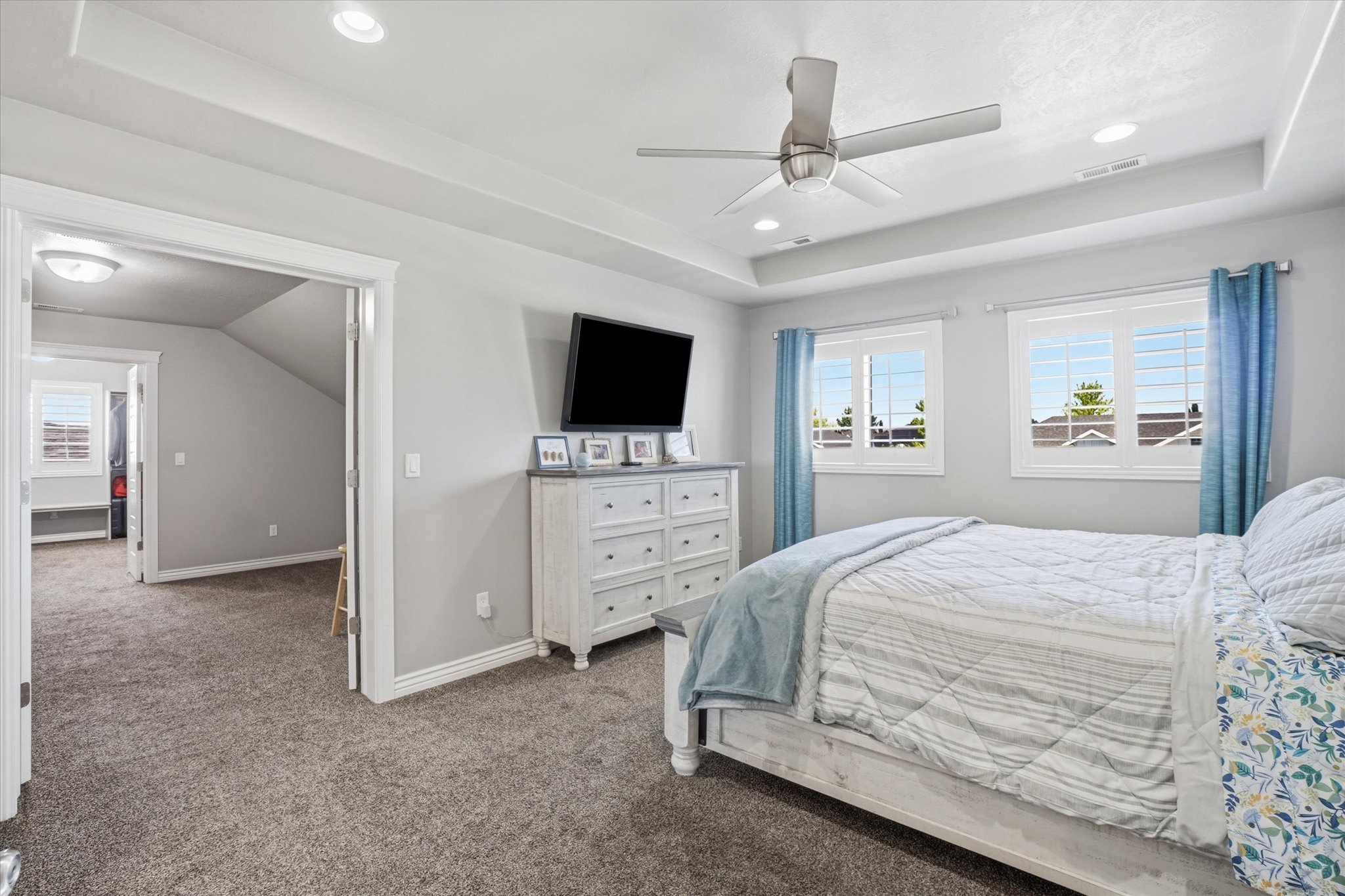 Spacious bedroom featuring neutral wall paint, plush carpeting, and a tray ceiling with recessed lighting