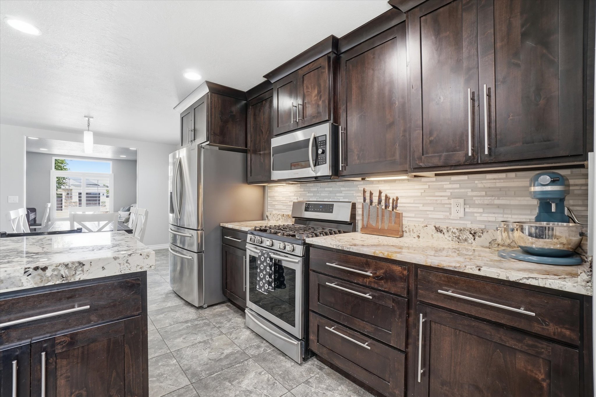 Kitchen featuring dark wood-finish cabinetry, light-toned granite countertops, and a mosaic tile backsplash