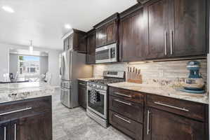 Kitchen featuring dark wood-finish cabinetry, light-toned granite countertops, and a mosaic tile backsplash