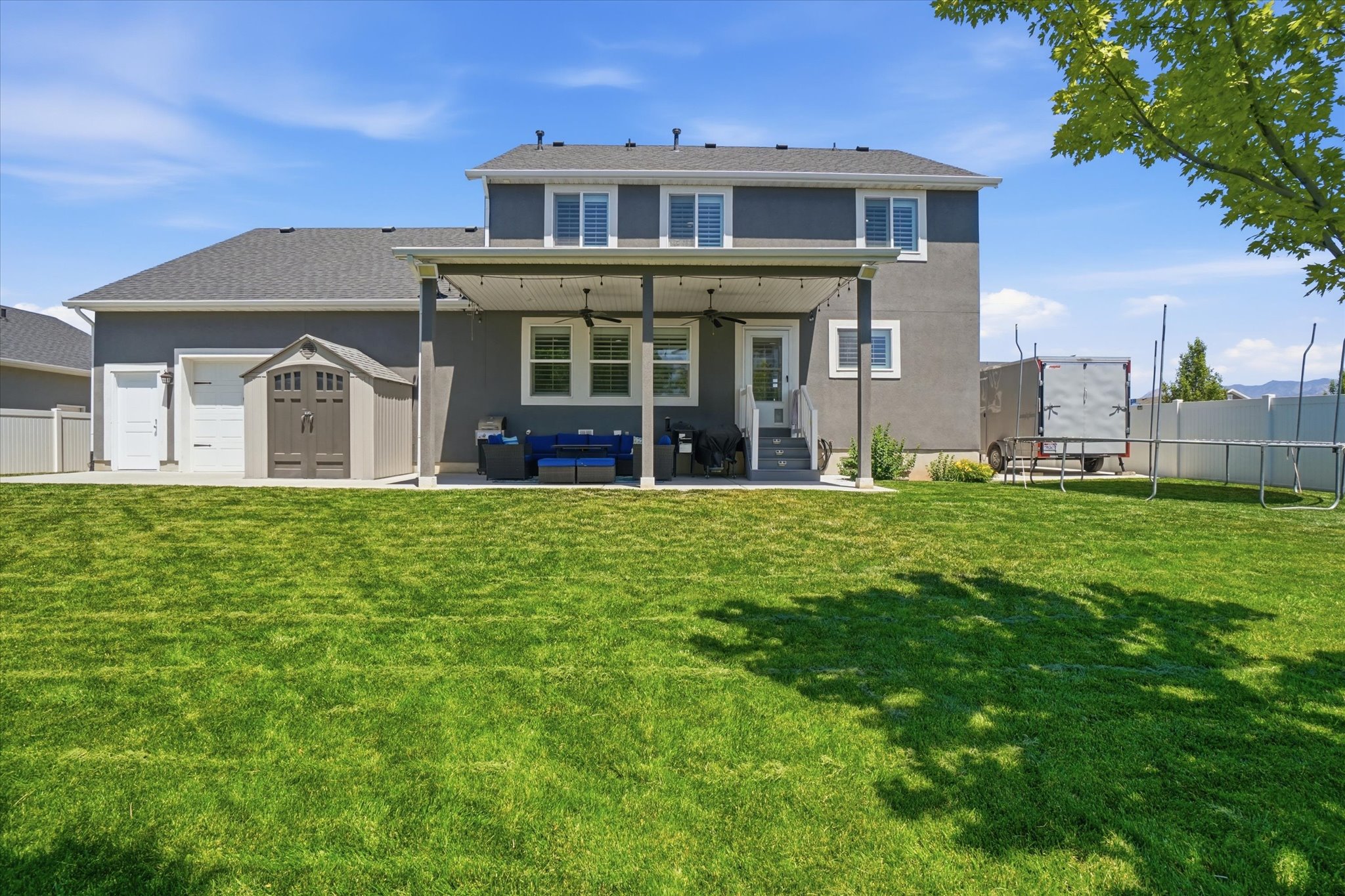 Expansive green lawn with a covered patio featuring recessed lighting and a ceiling fan
