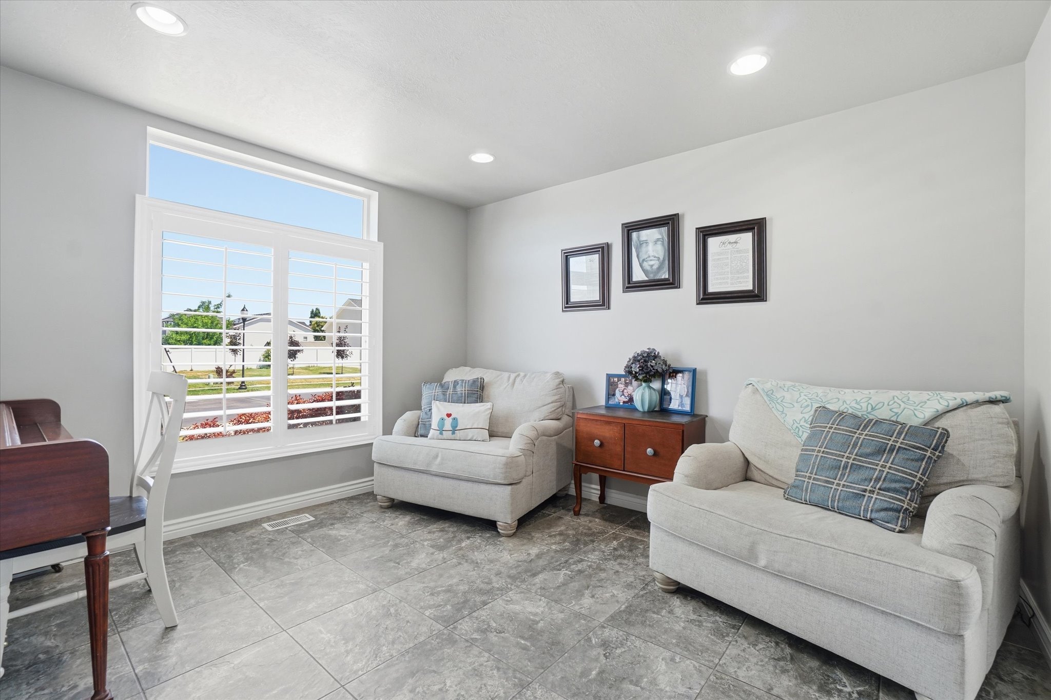 Spacious room featuring a large window with transom, white window shutters, recessed lighting, light gray walls, and gray tile flooring