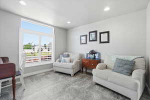 Spacious room featuring a large window with transom, white window shutters, recessed lighting, light gray walls, and gray tile flooring