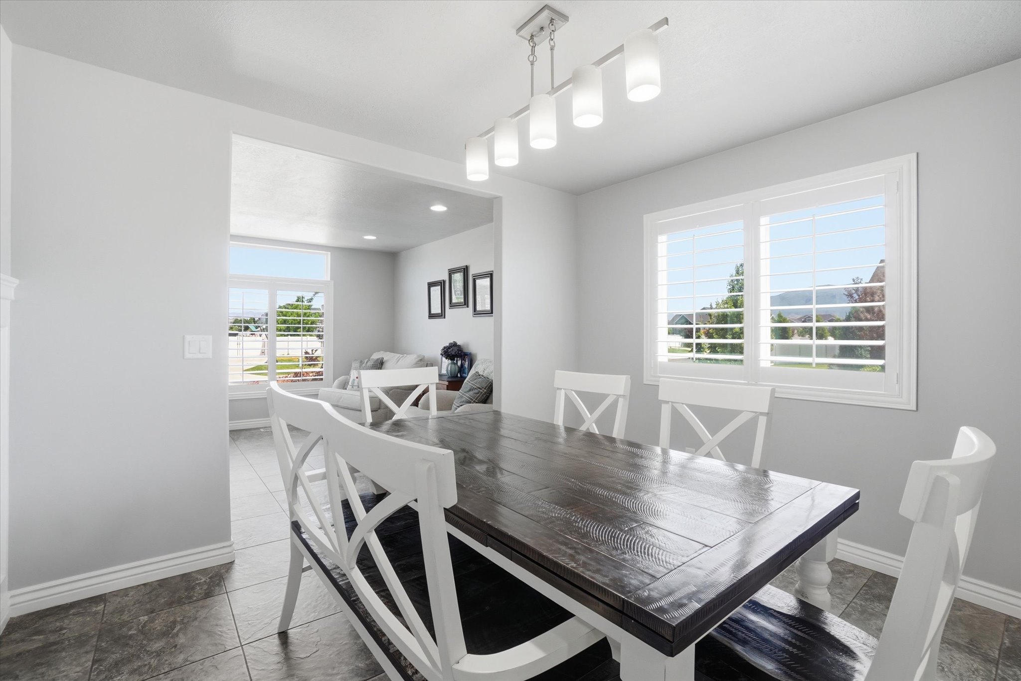 Dining area featuring a contemporary linear chandelier, tiled flooring, and windows with white plantation shutters