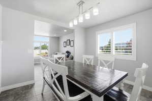 Dining area featuring a contemporary linear chandelier, tiled flooring, and windows with white plantation shutters