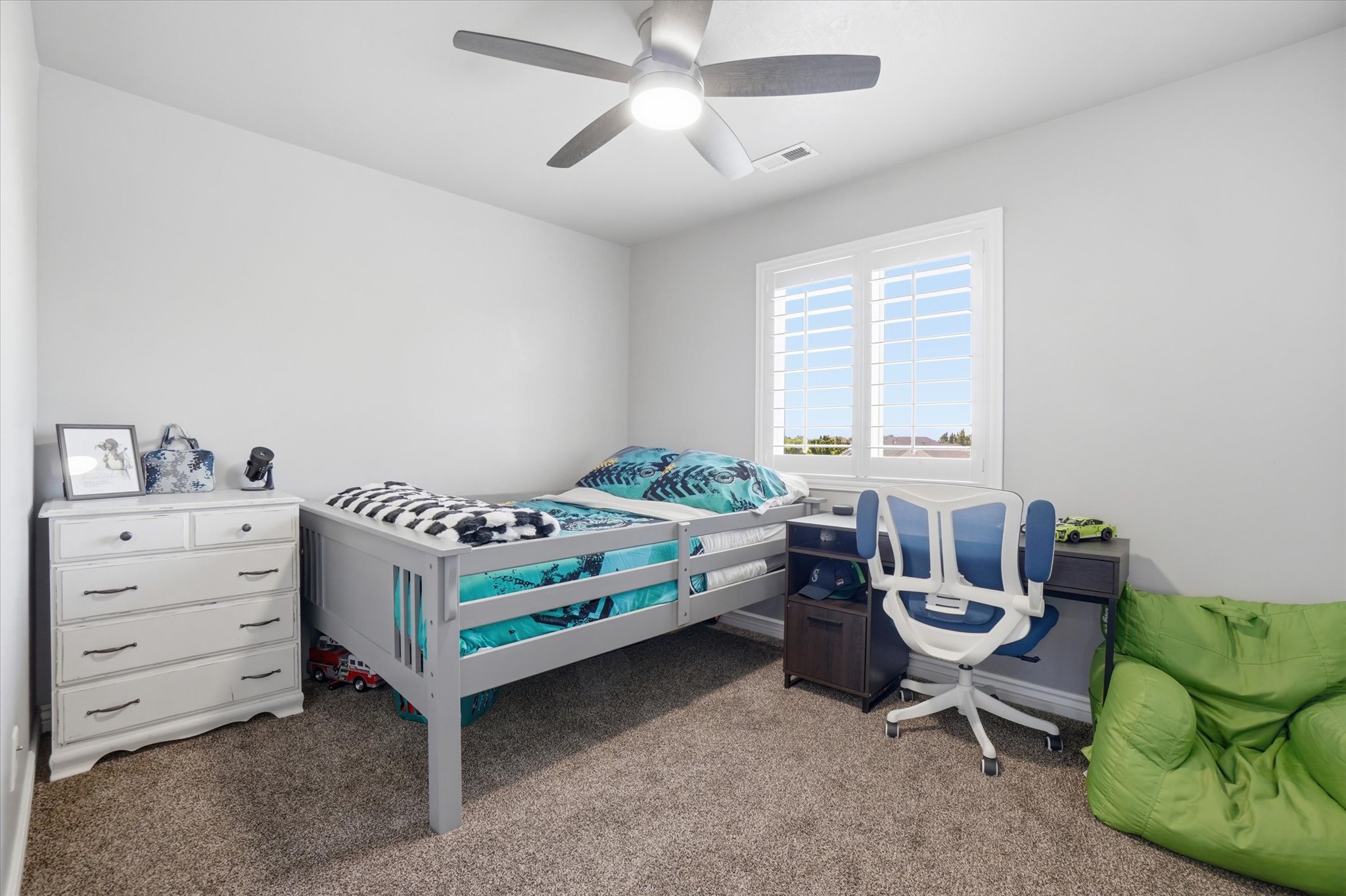 Carpeted room featuring a ceiling fan with integrated lighting, a window with plantation shutters, and a built-in desk with cabinetry