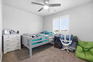 Carpeted room featuring a ceiling fan with integrated lighting, a window with plantation shutters, and a built-in desk with cabinetry