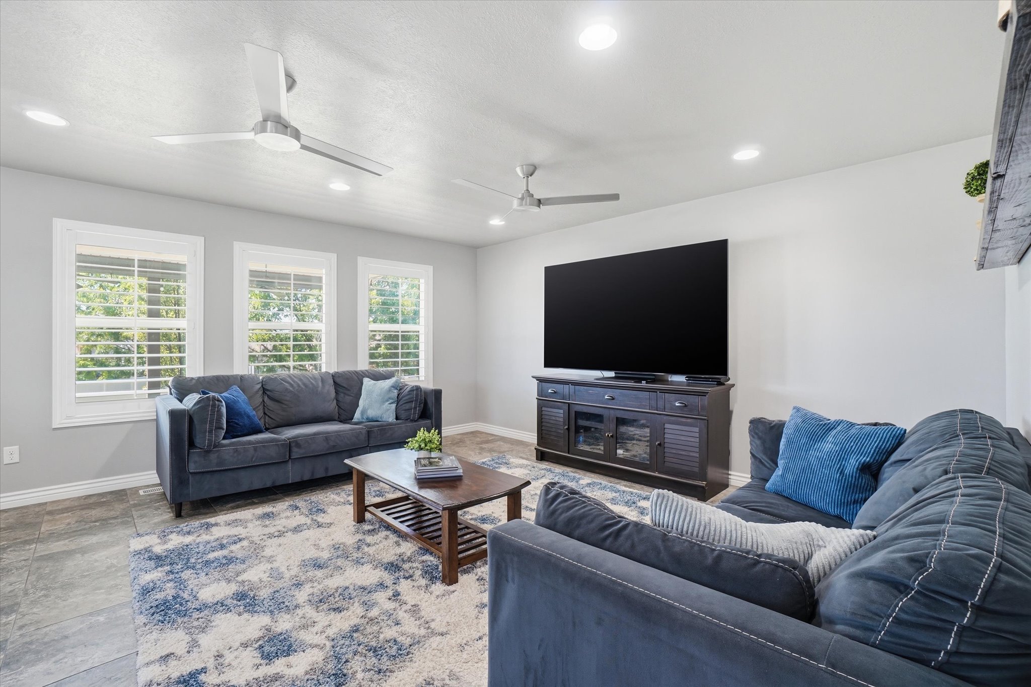 Expansive living area featuring three large windows with plantation shutters, recessed lighting, and two ceiling fans