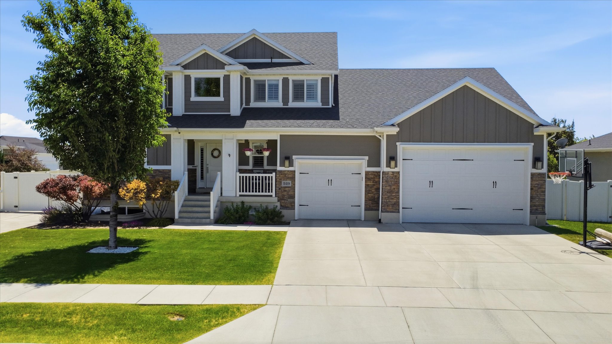 Modern two-story residence featuring a covered front porch with white railing, a two-car garage with carriage-style doors, and a stone accent facade