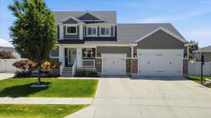 Modern two-story residence featuring a covered front porch with white railing, a two-car garage with carriage-style doors, and a stone accent facade