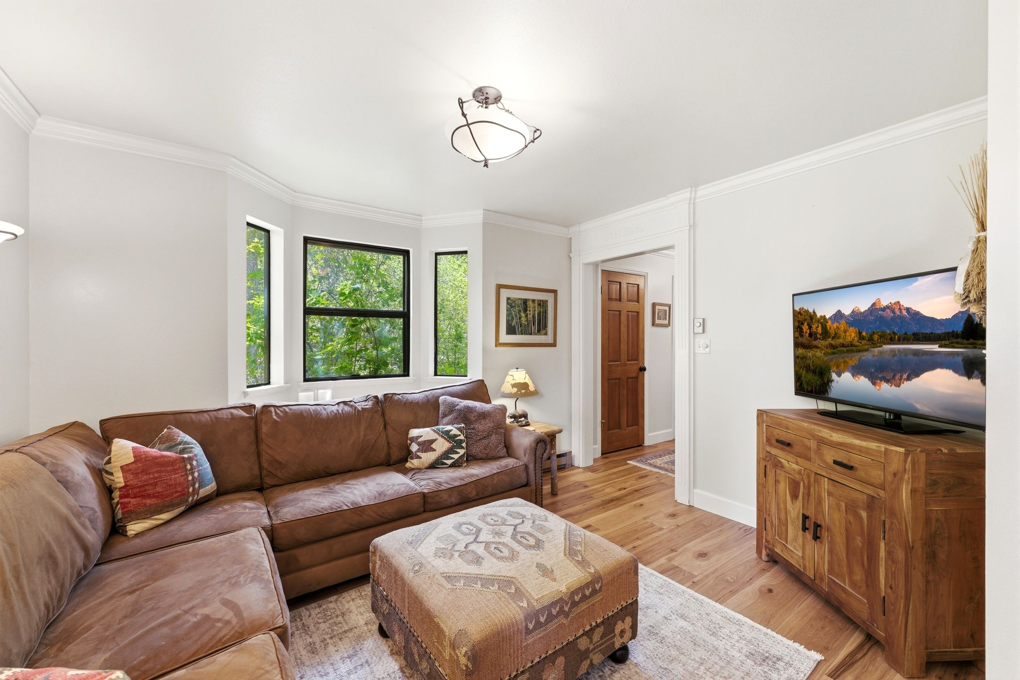 Living area featuring wood-finish flooring, a bay window with black frames, white crown molding, and a paneled wood door