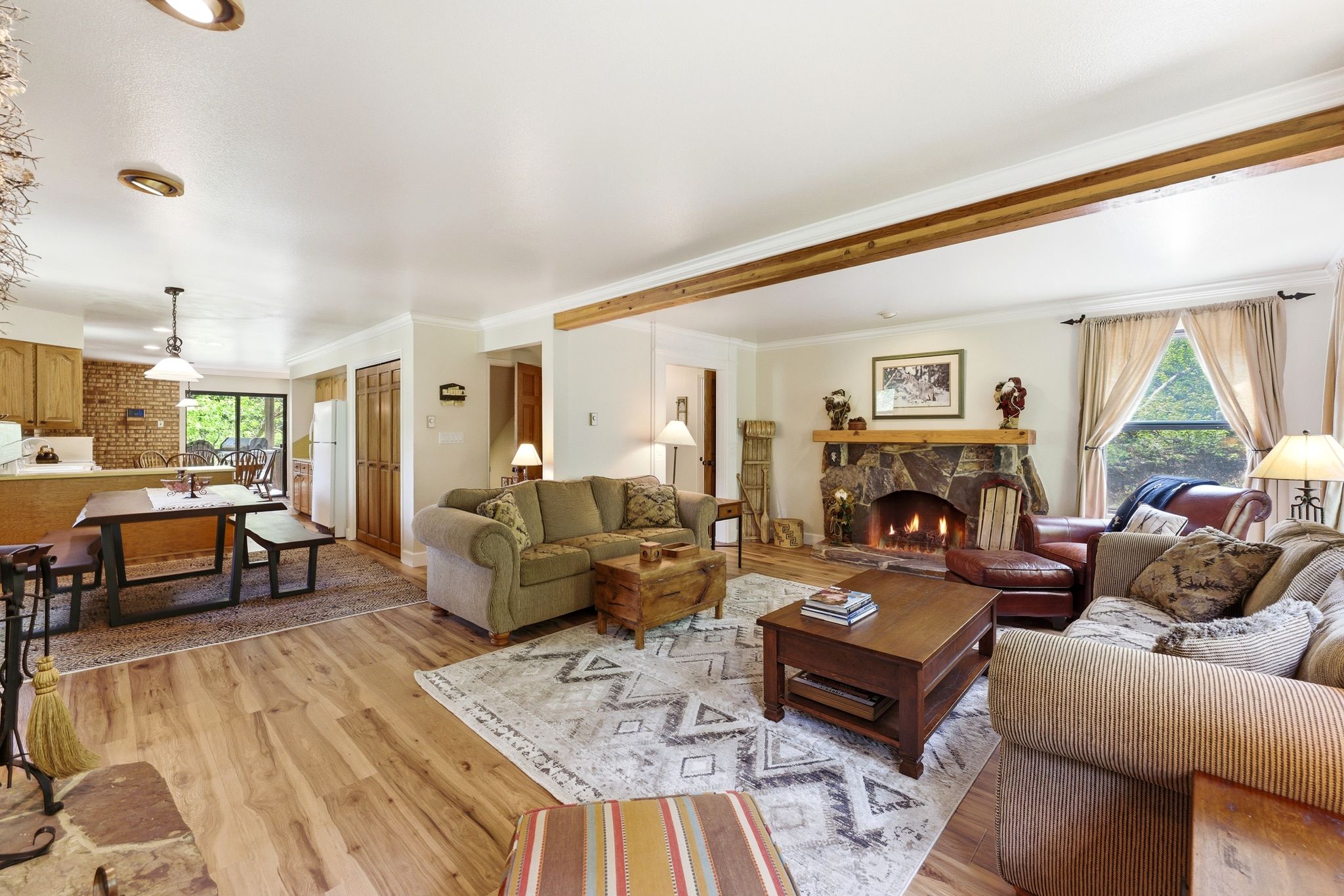 Living area featuring a stone fireplace with a wood mantle, wood-finish flooring, and exposed ceiling beams