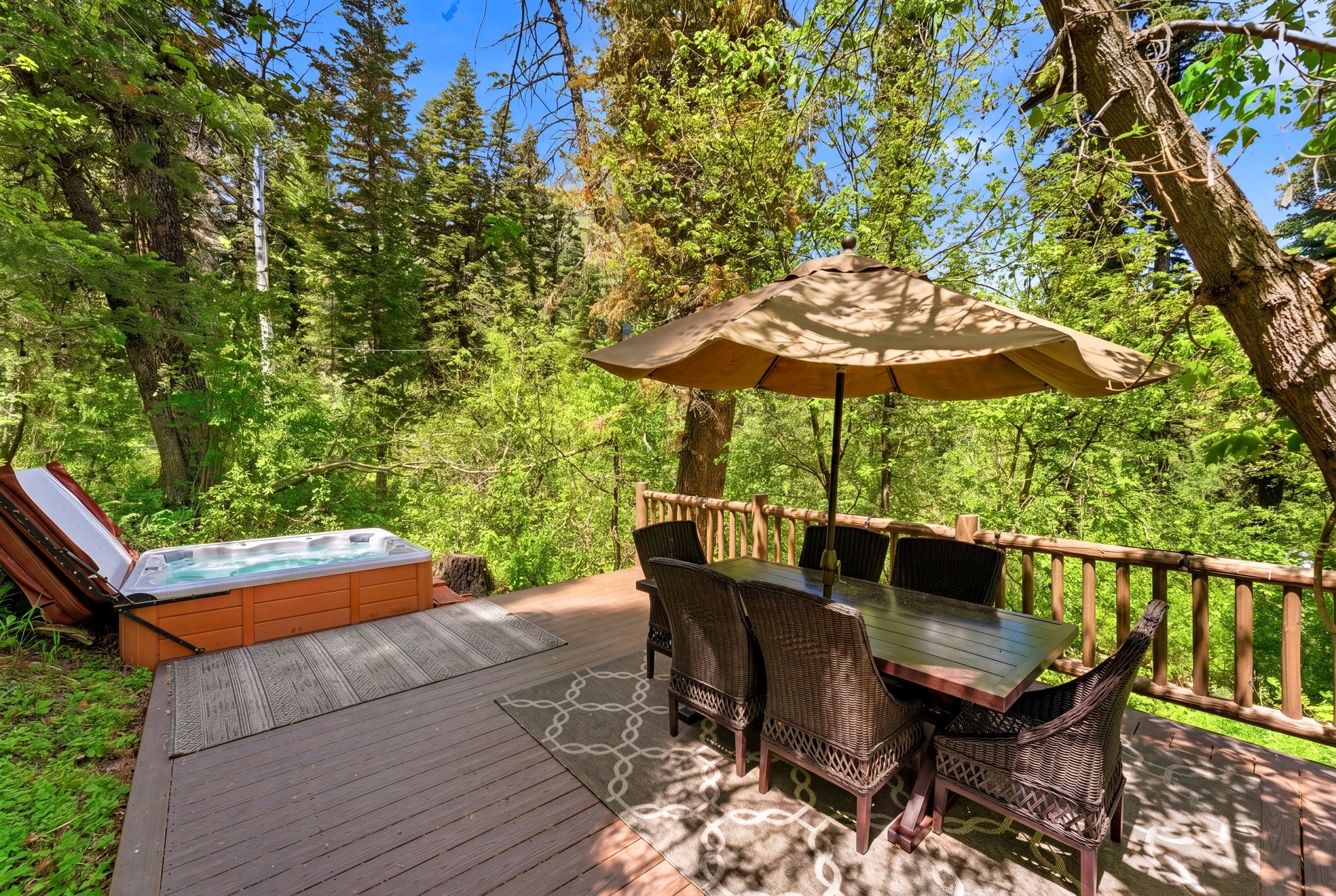 Outdoor wood-finish deck featuring a built-in hot tub, a natural wood railing, and a dining area