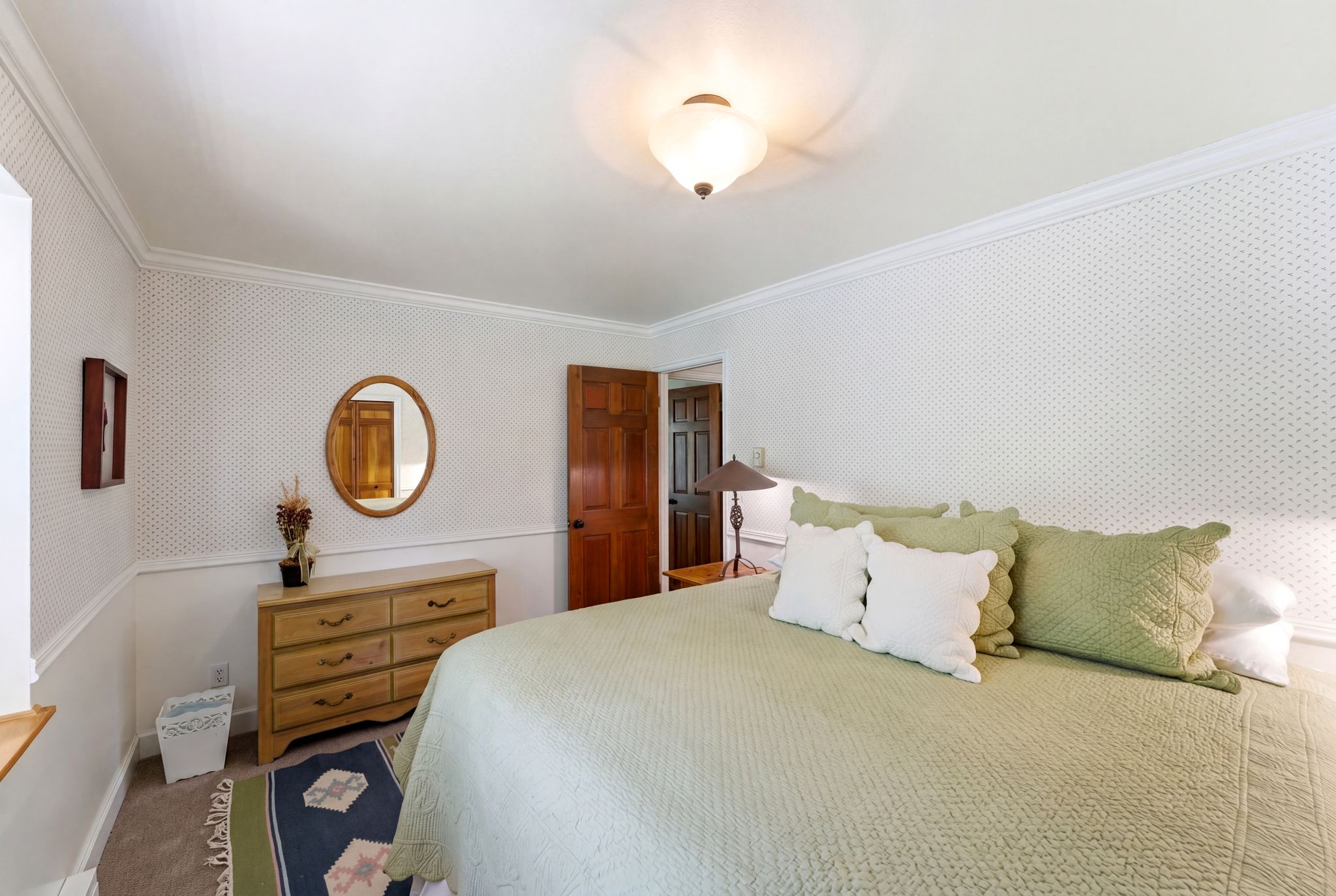 Bedroom featuring patterned wallpaper, white crown molding, and a warm wood-finish door