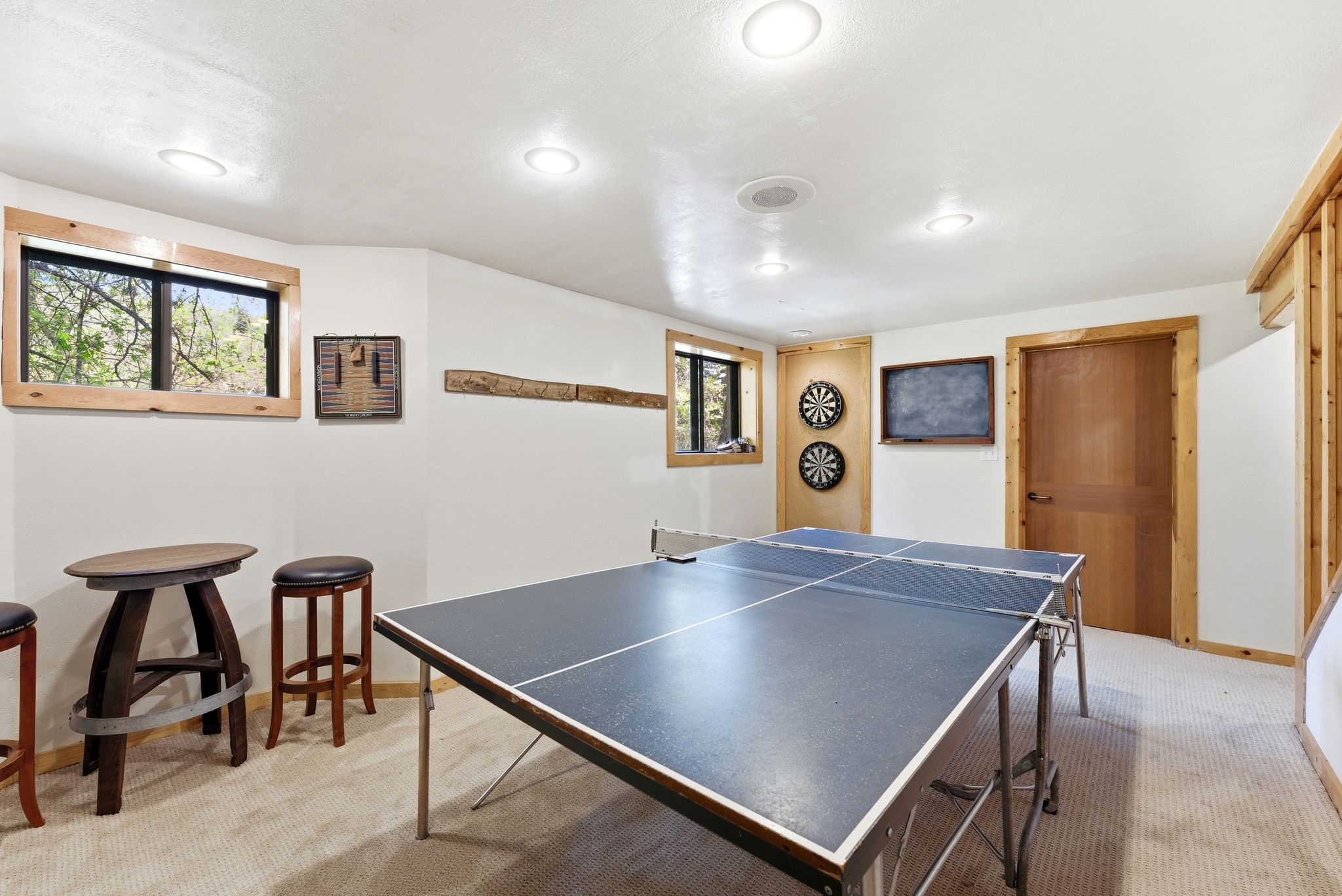 Recessed lighting illuminates a carpeted recreation room featuring natural wood trim around windows and a solid wood door