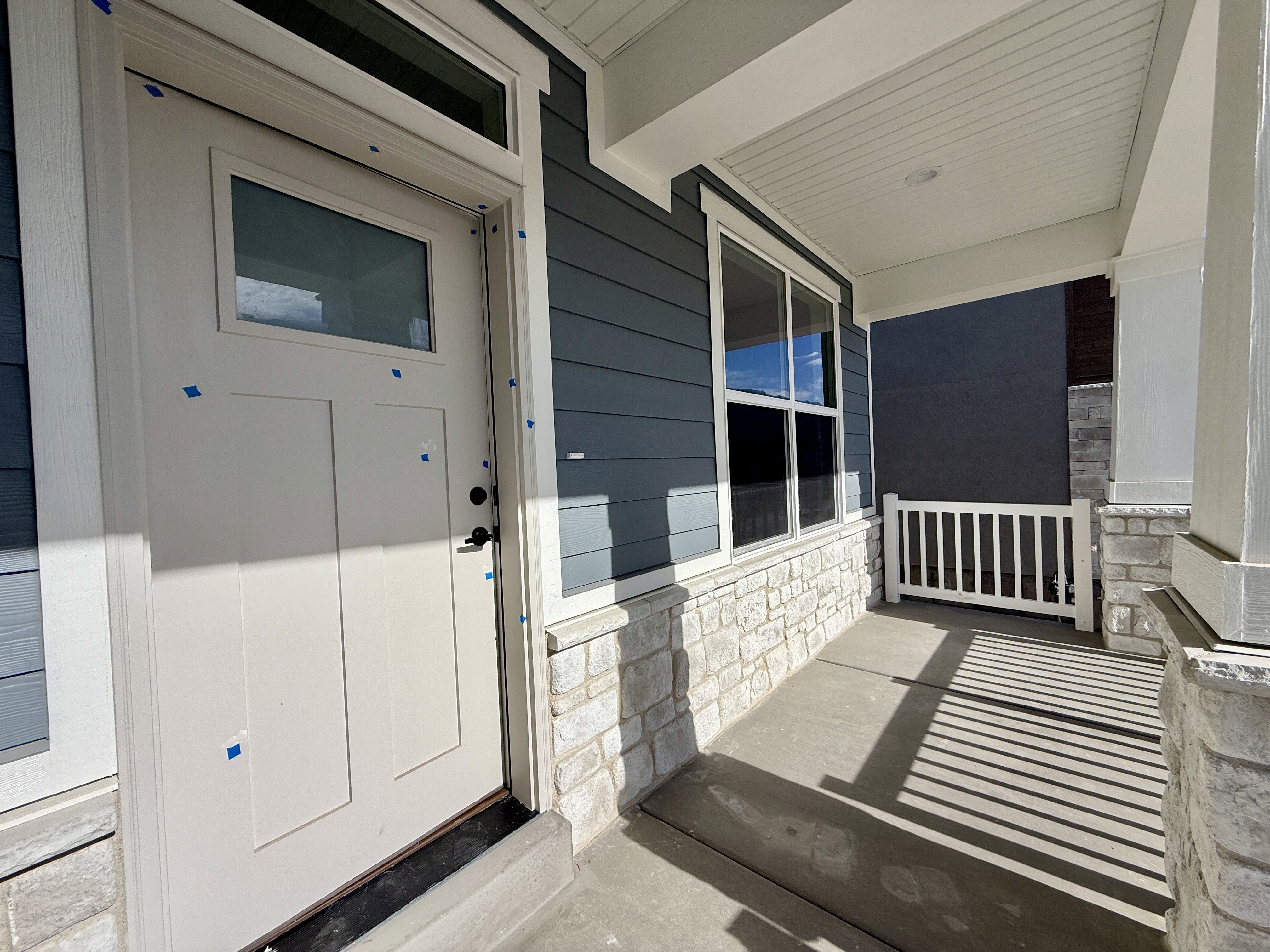 Covered front porch featuring a paneled entry door with transom window, horizontal siding, stone veneer, and white balusters