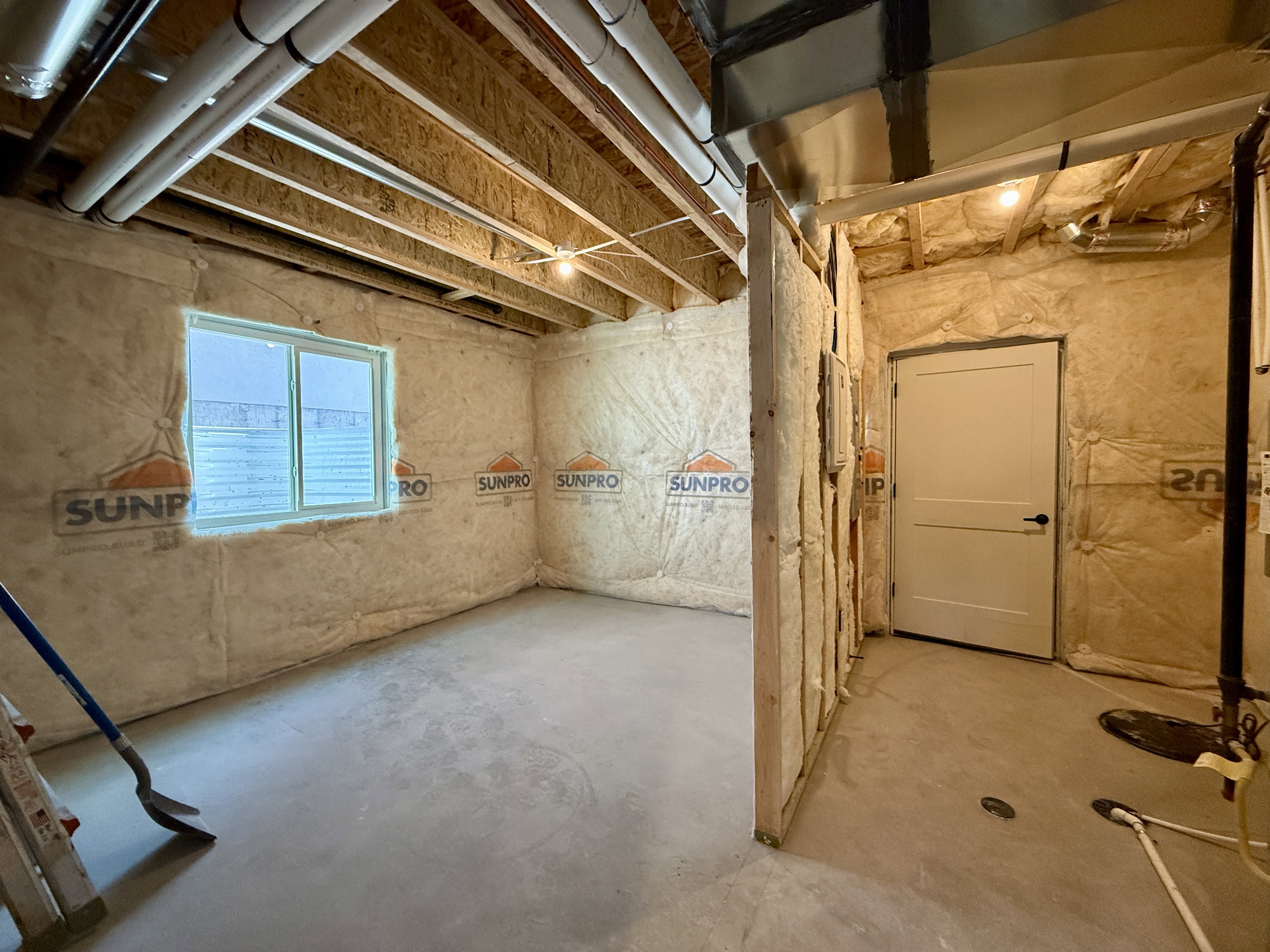 Unfinished basement space featuring a window, exposed ceiling joists, insulation, concrete flooring, and a white interior door