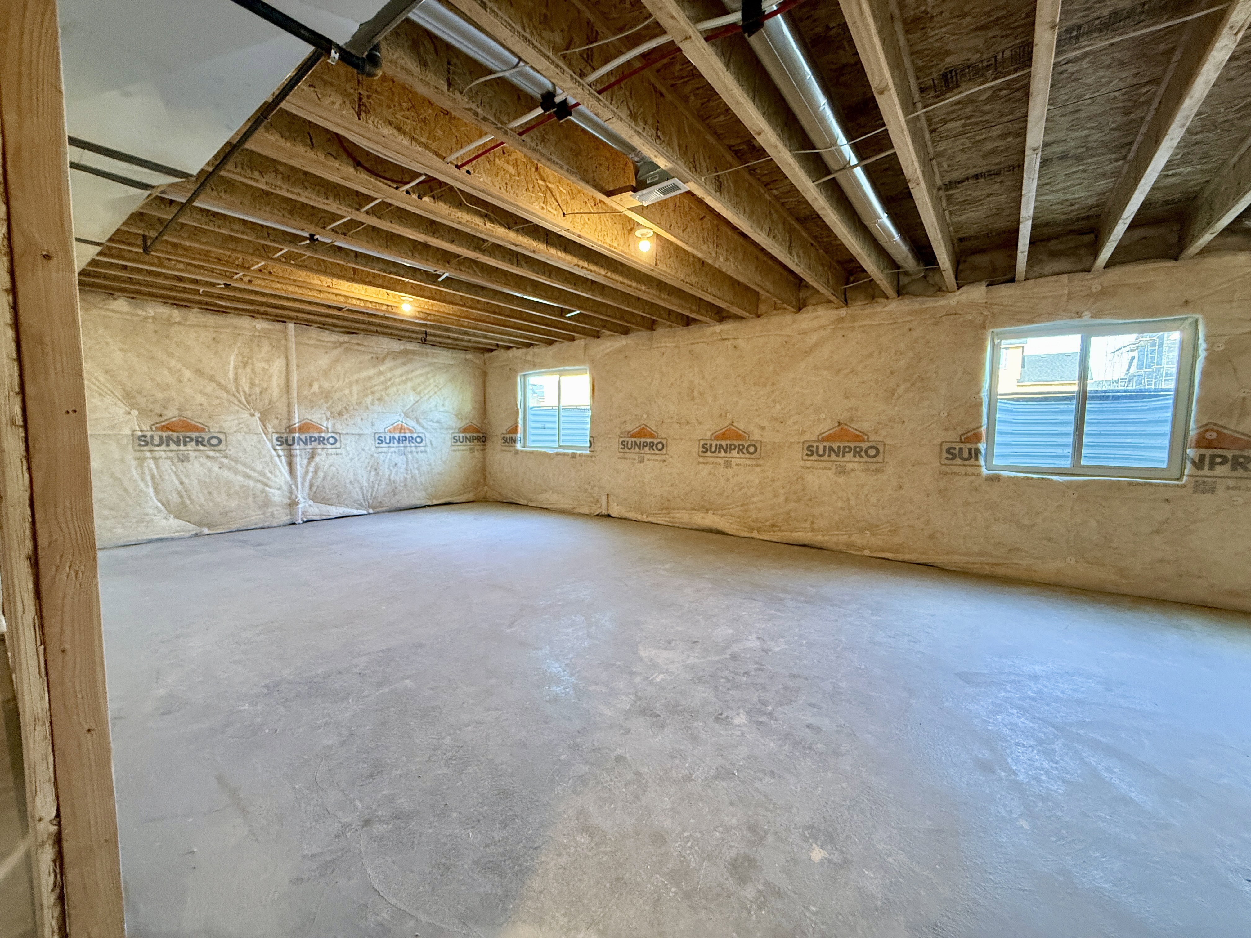 Unfinished basement featuring exposed wood joists, concrete flooring, and two windows