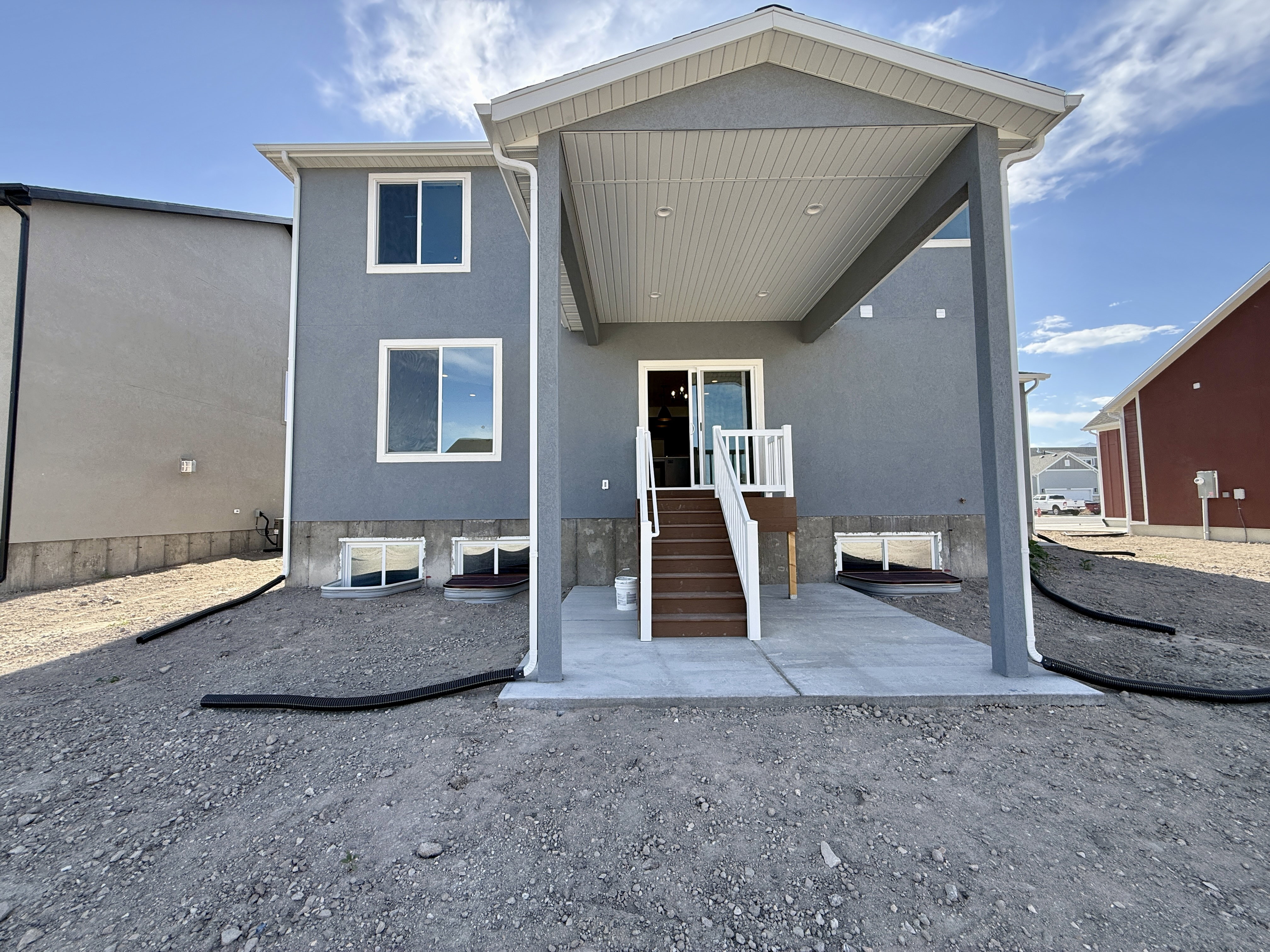 Rear exterior featuring a covered patio, concrete slab, and wood-finish stairs with white railing