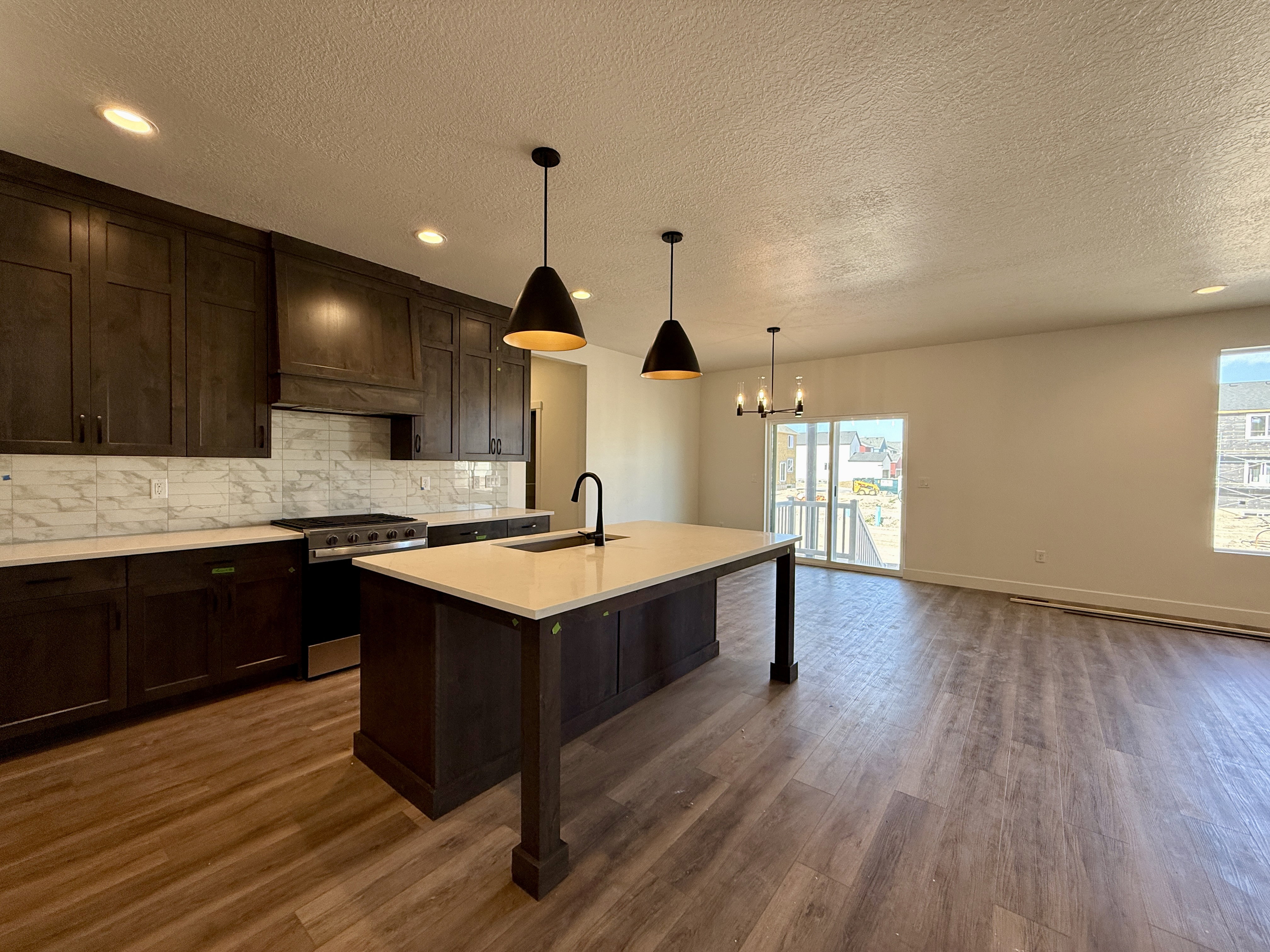 Open-concept kitchen featuring dark wood cabinetry, white countertops, and a full tile backsplash