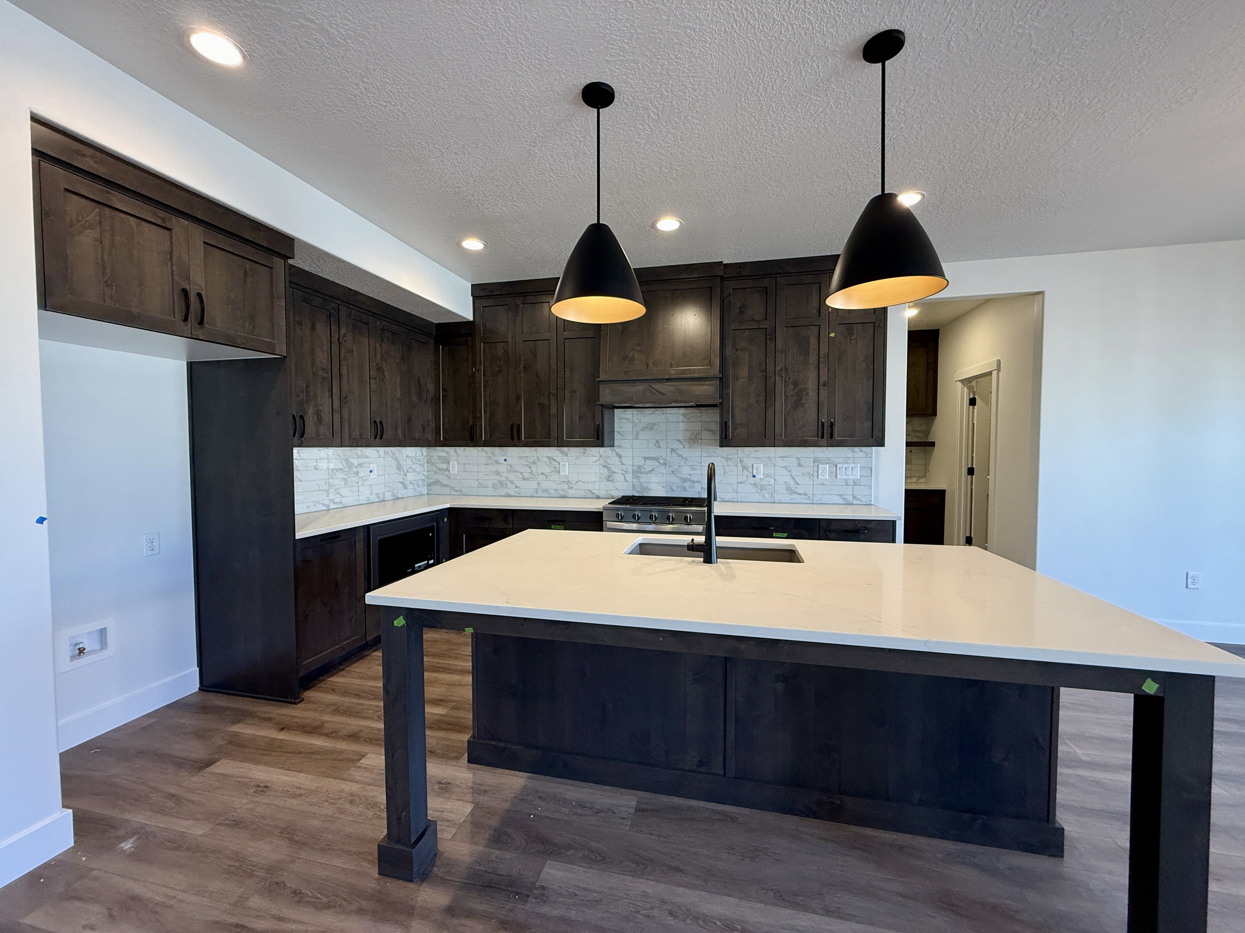 Contemporary kitchen island featuring a light-toned countertop, dark wood-finish cabinetry, and two matte black pendant lights