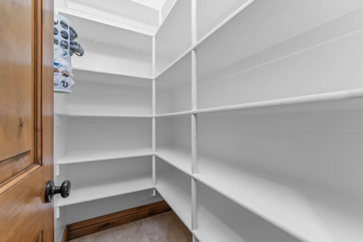 Walk-in pantry featuring expansive white shelving, wood-finish baseboard, and light tile flooring