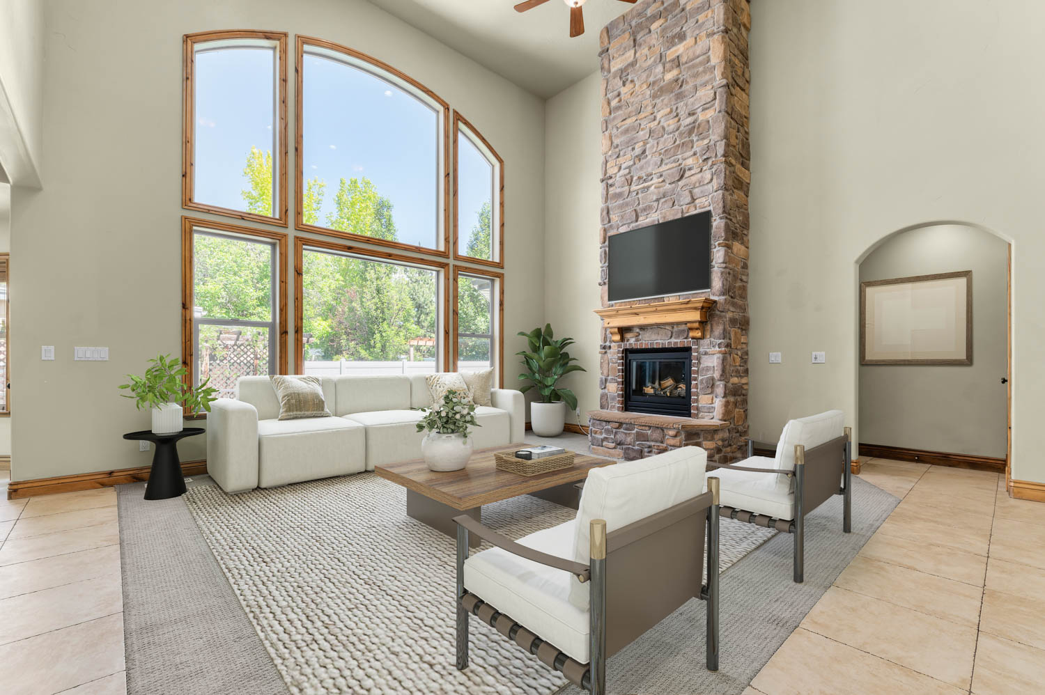 Living area featuring a floor-to-ceiling stone fireplace, arched window frames, high ceilings, and wood-finish flooring
