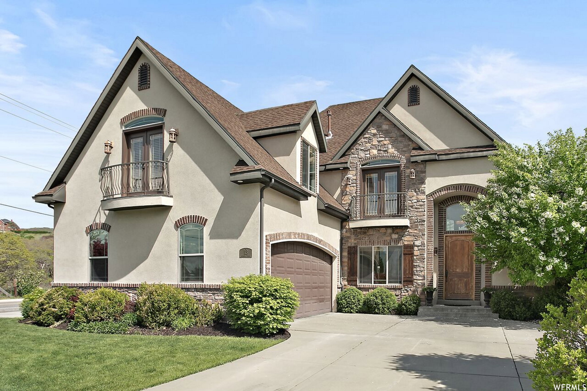 Stucco and stone exterior featuring an arched wood-panel entry door, an arched garage door, decorative iron balconies, and a paved driveway
