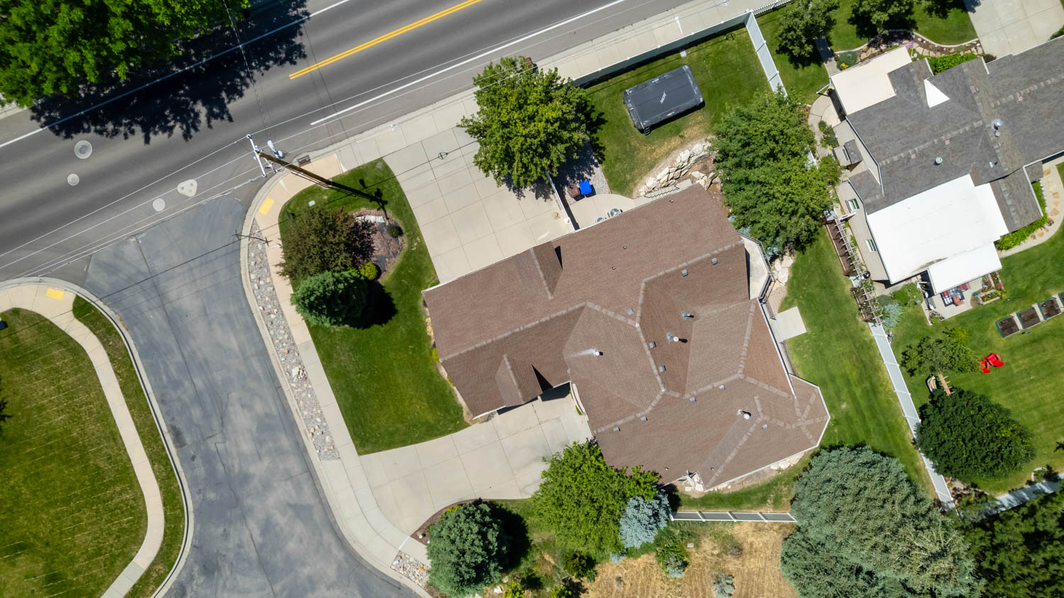 Expansive corner lot featuring a brown shingle roof, concrete driveway, and mature landscaping