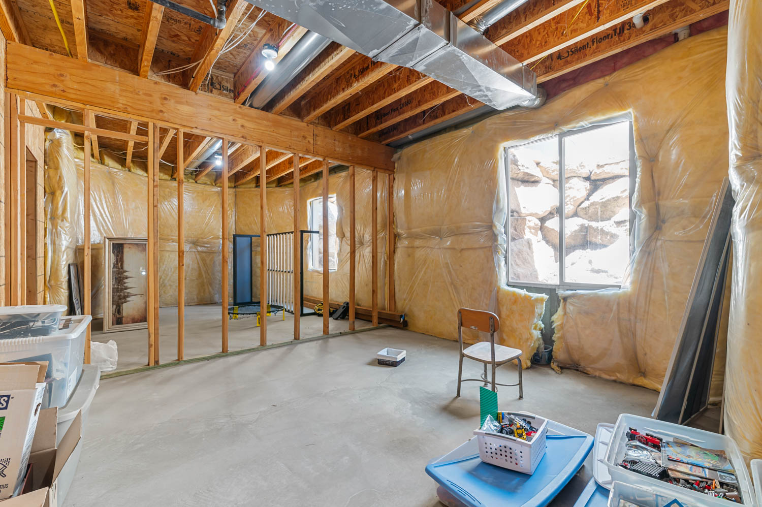 Unfinished basement space featuring exposed wooden ceiling joists, concrete flooring, and framed interior walls