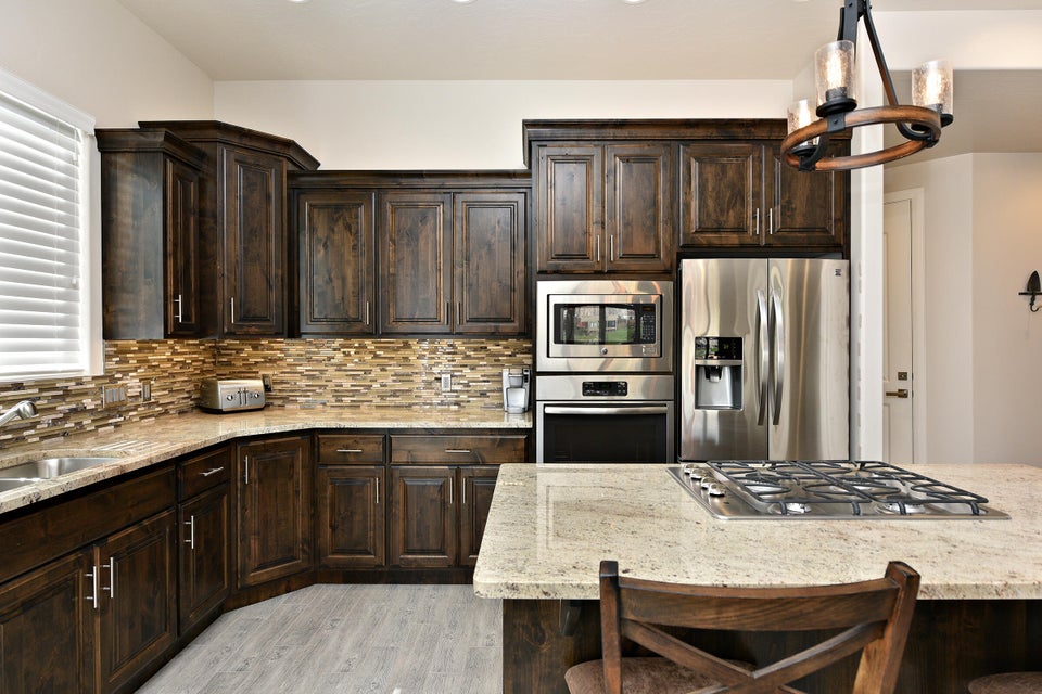 Kitchen featuring dark wood cabinetry, light-toned countertops, stainless steel appliances, and a mosaic tile backsplash