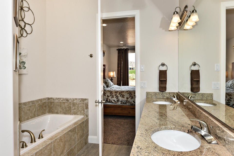 Bathroom featuring a built-in soaking tub with brass fixtures, a dual vanity with light-toned stone countertop, integrated sinks, and a large mirror