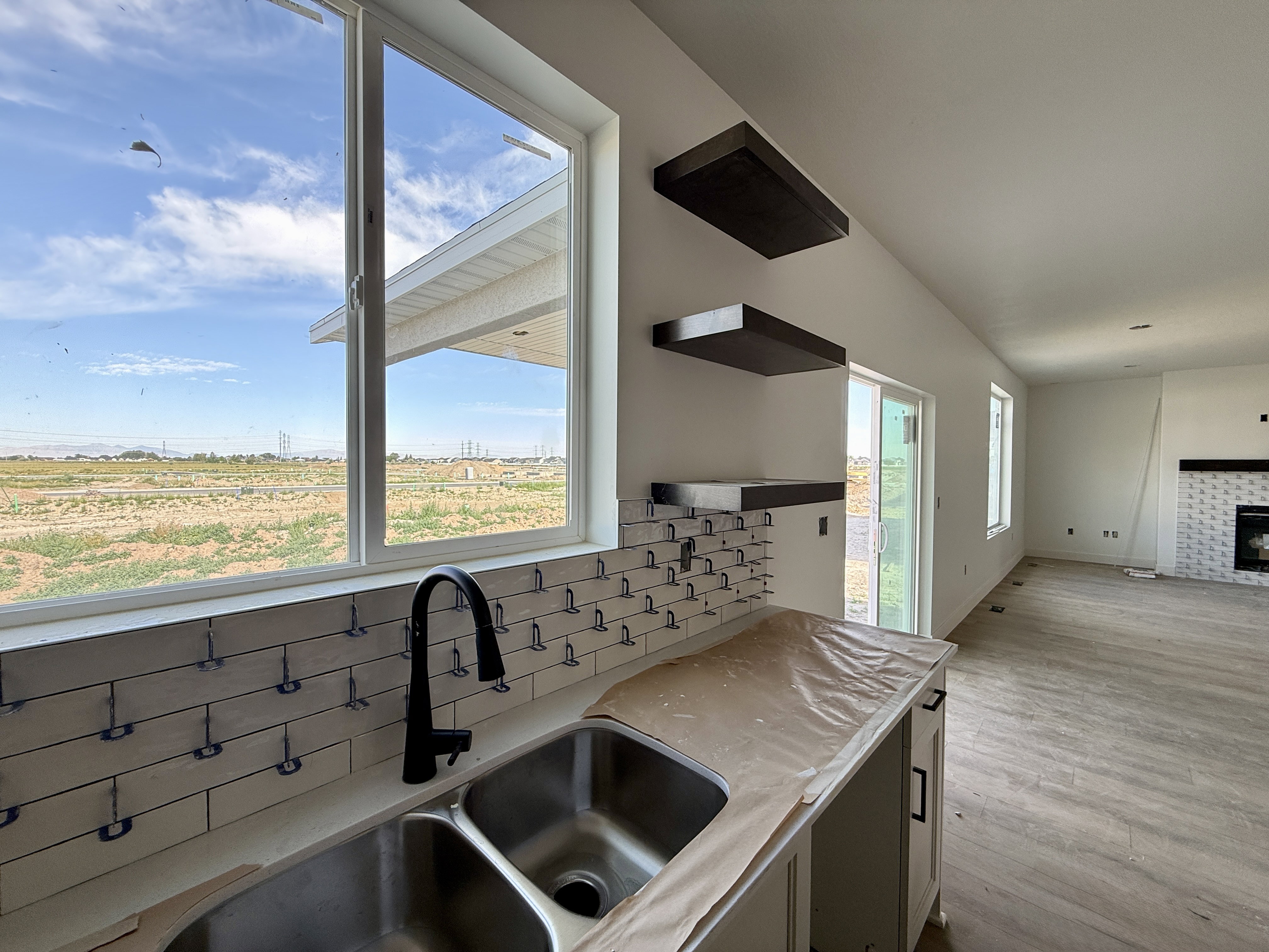 Kitchen space featuring a double basin stainless steel sink with a matte black faucet, subway tile backsplash, and light-colored cabinetry with dark hardware