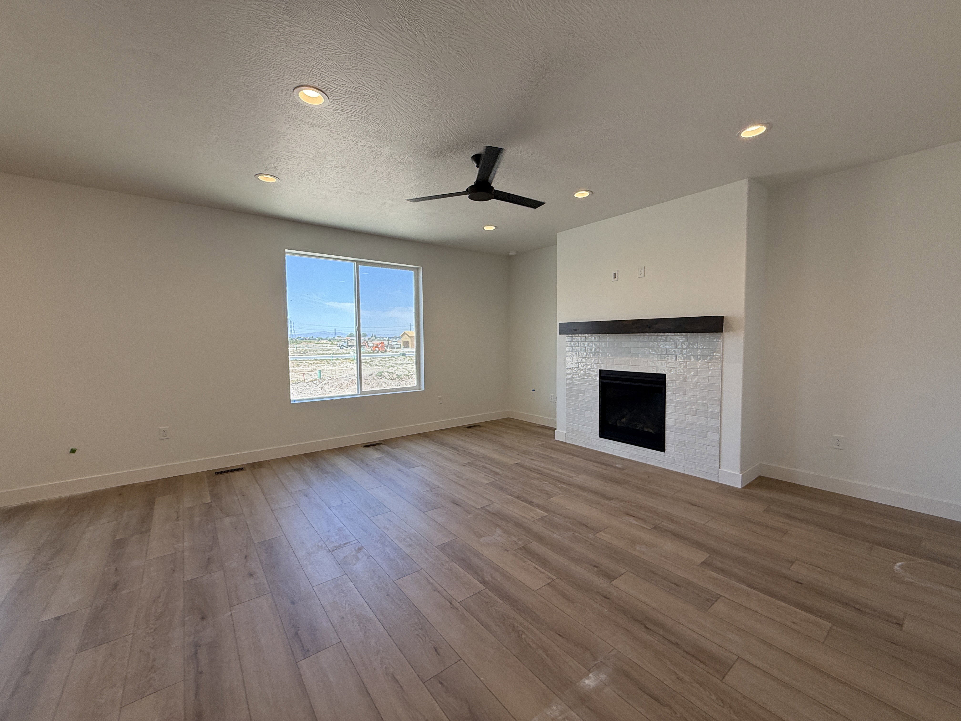 Spacious room featuring wood-finish flooring, a contemporary fireplace with white tile surround and dark wood mantel, recessed lighting, and a modern ceiling fan