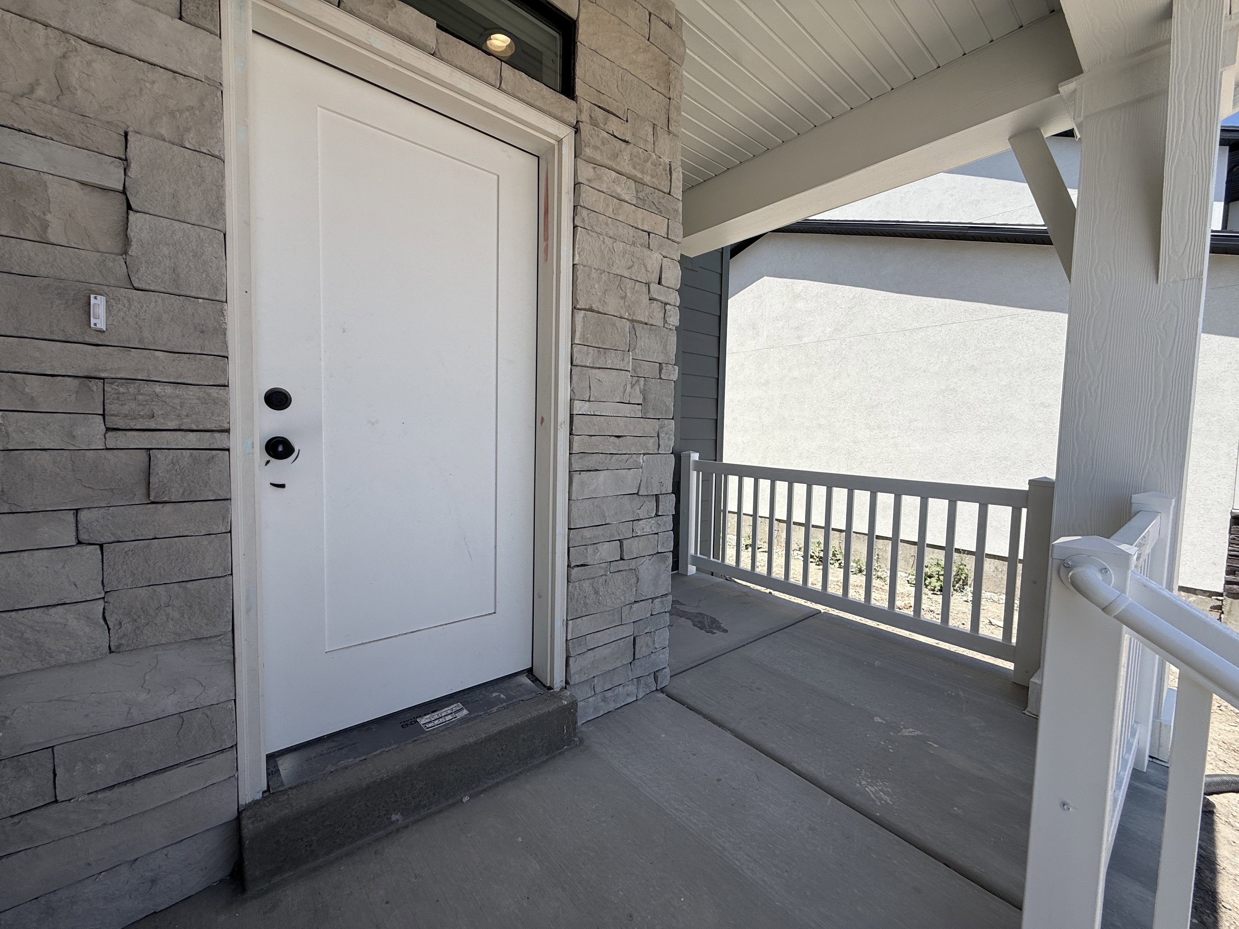 Entryway featuring stone veneer facade, white paneled door, transom window, covered porch, and white railing