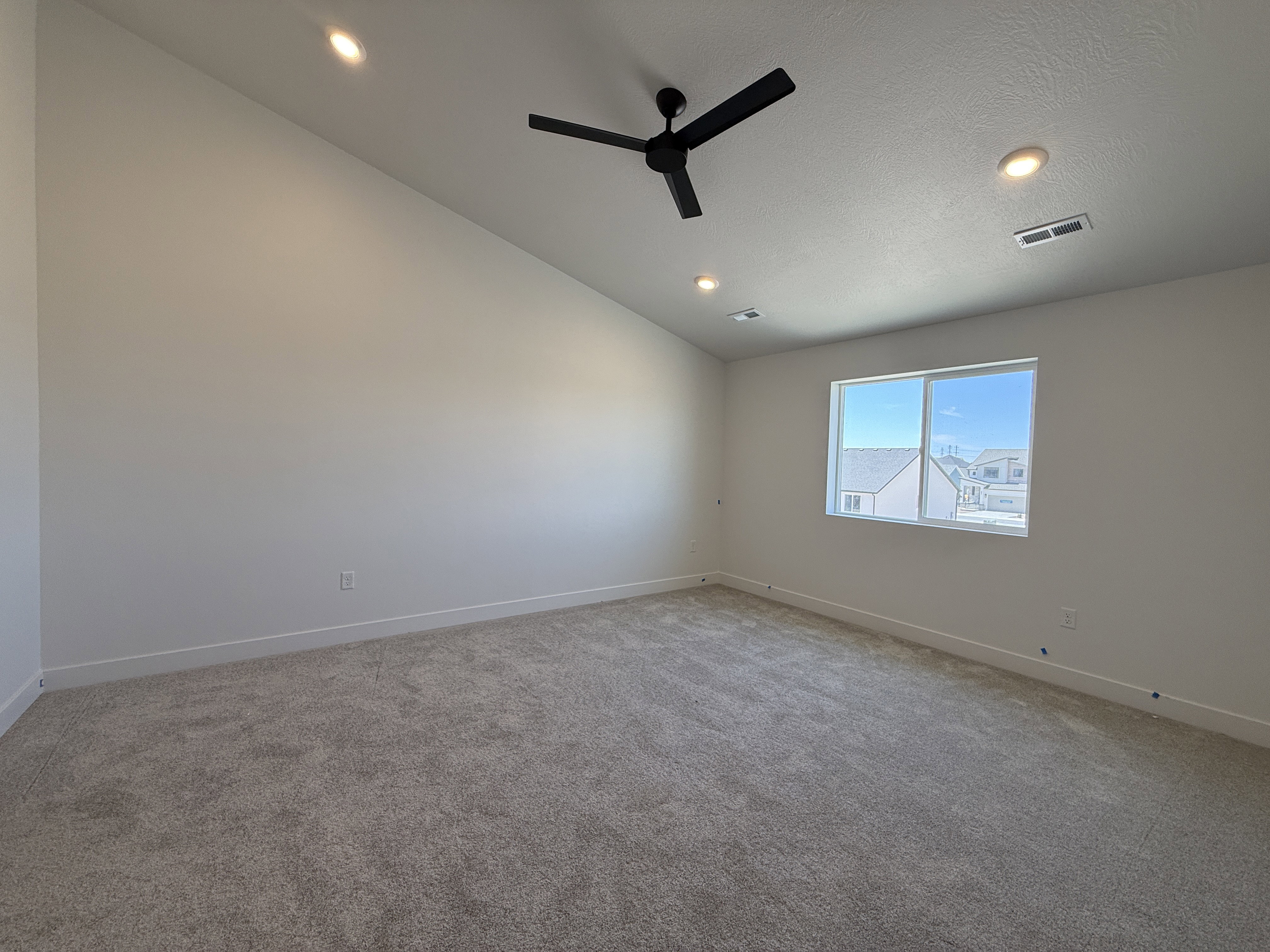 Spacious room featuring vaulted ceilings, recessed lighting, a modern black ceiling fan, light gray carpeting, and a large window providing natural illumination