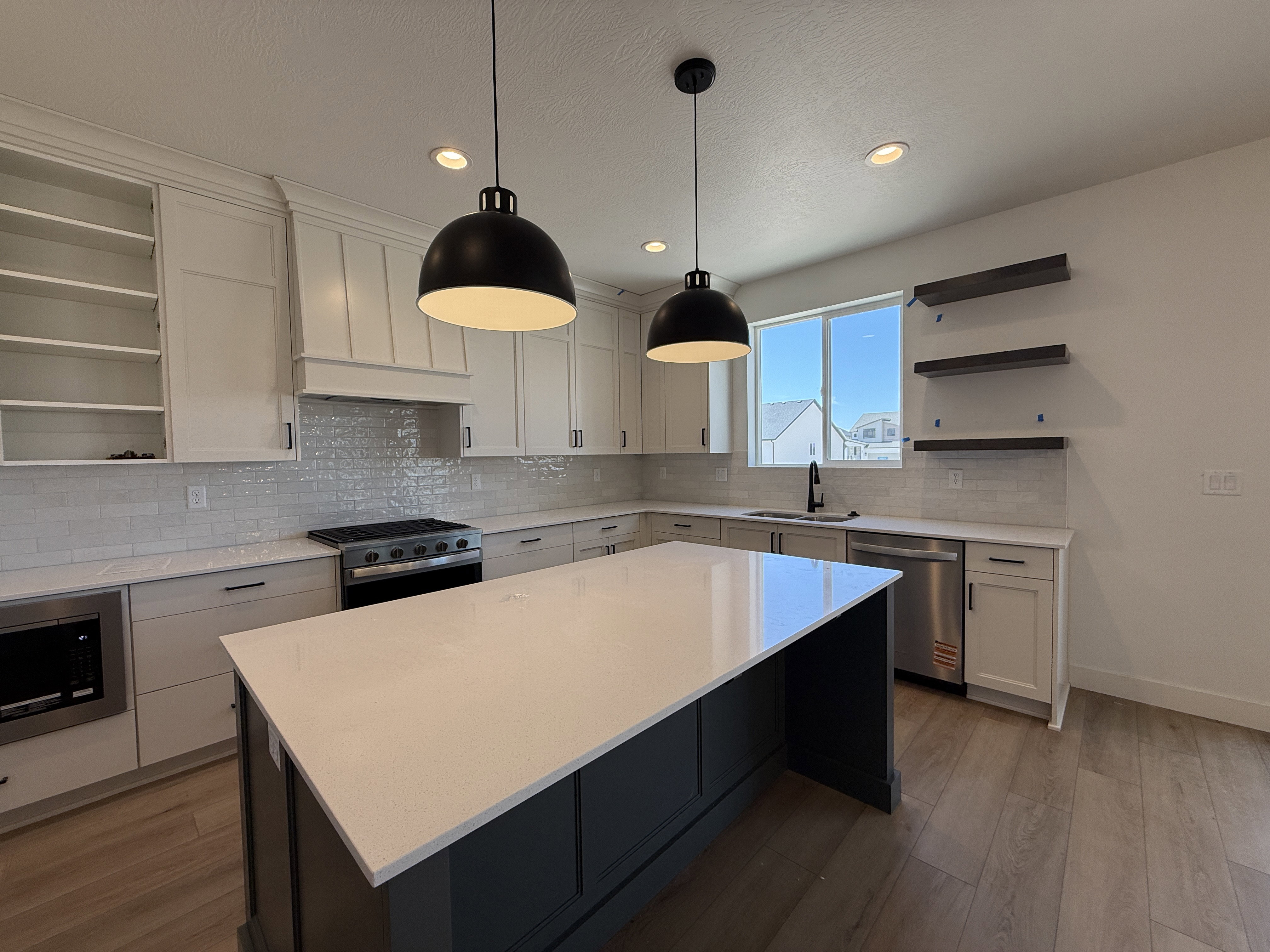 Contemporary kitchen featuring a large central island with a light-toned countertop, white cabinetry with dark hardware, a stainless steel gas range, and a subway tile backsplash