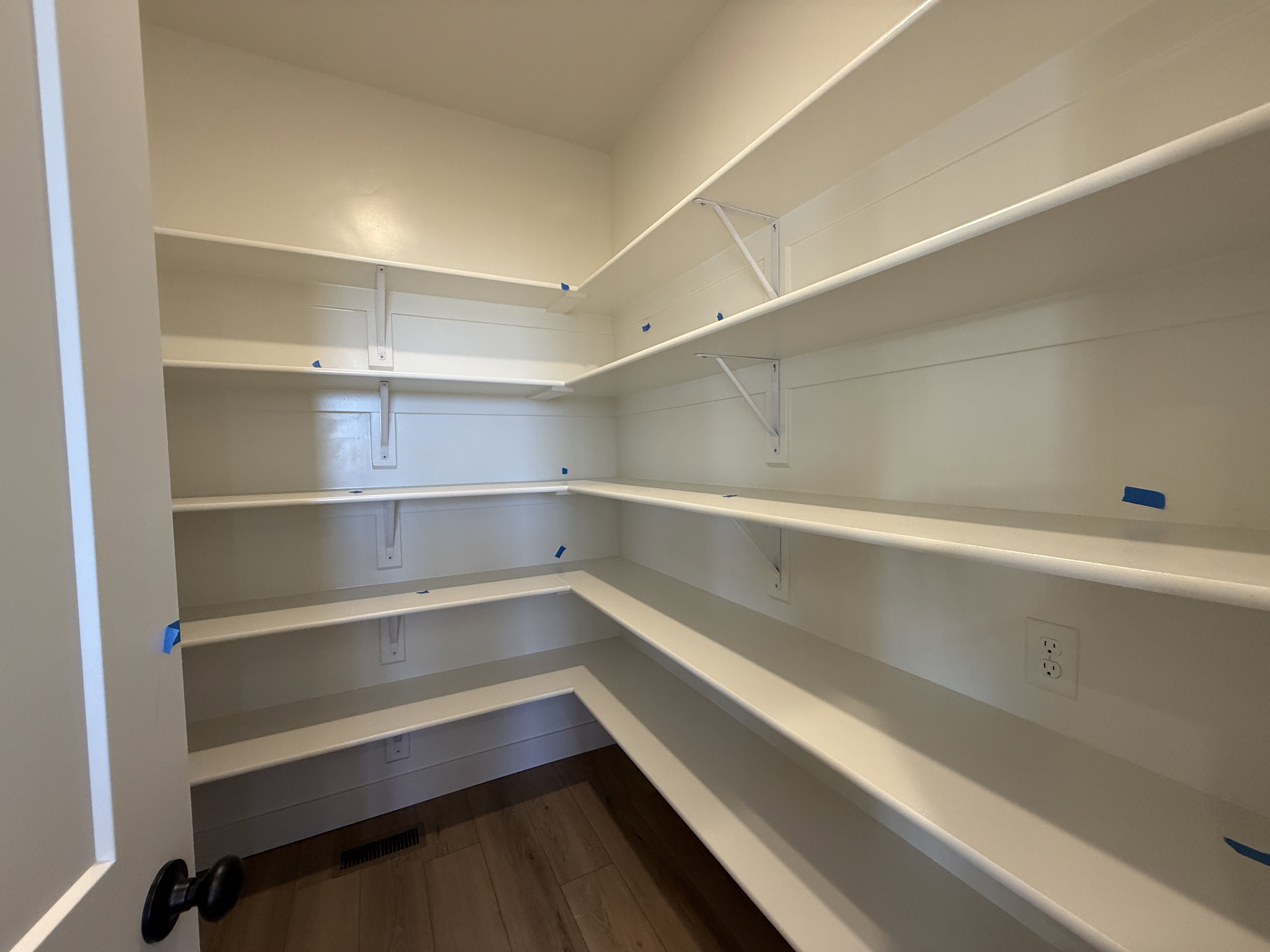 Walk-in pantry featuring extensive white shelving, wood-finish flooring, and multiple wall outlets