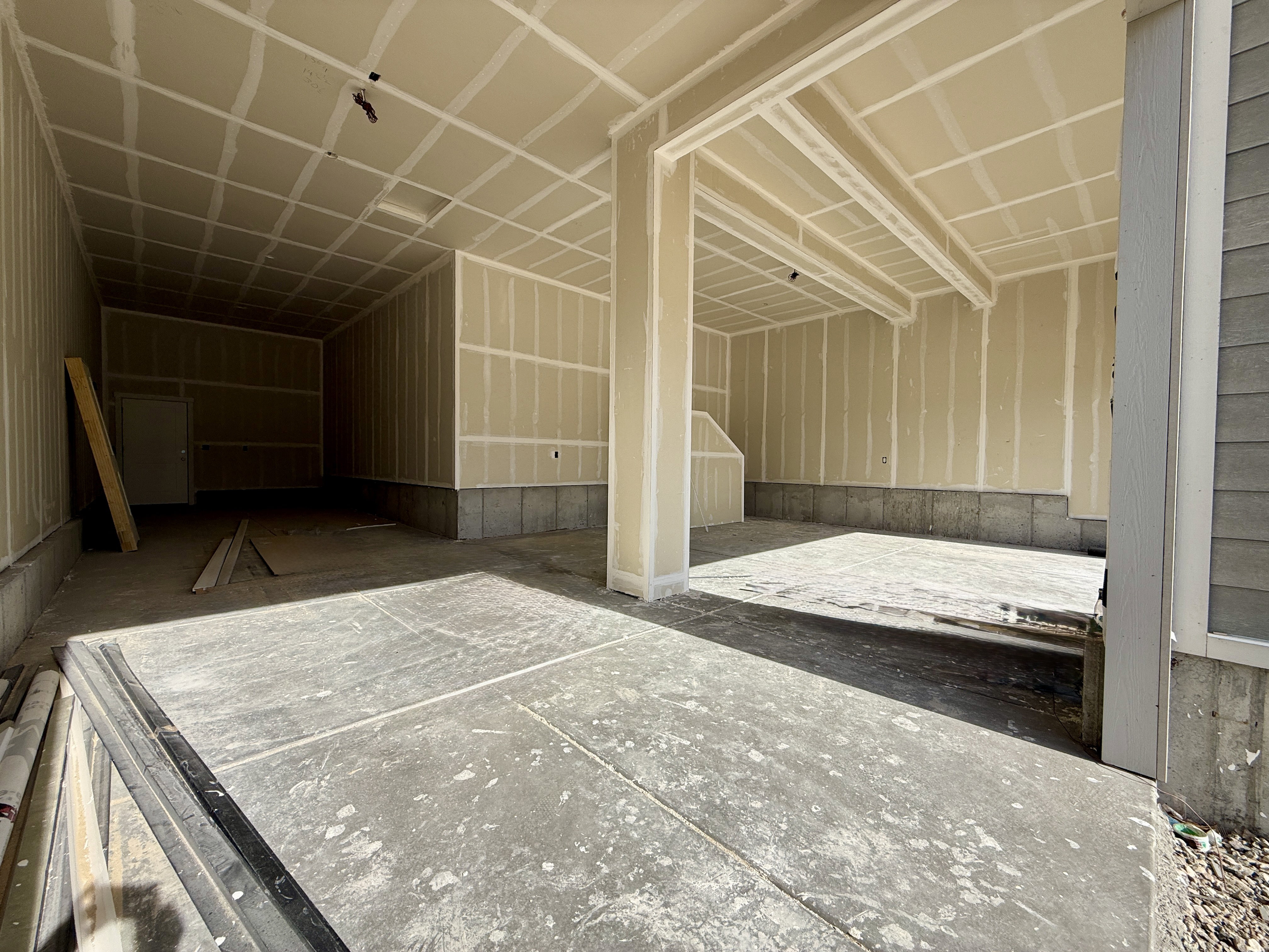 Spacious garage interior featuring concrete flooring, unpainted drywall walls, and exposed ceiling joists
