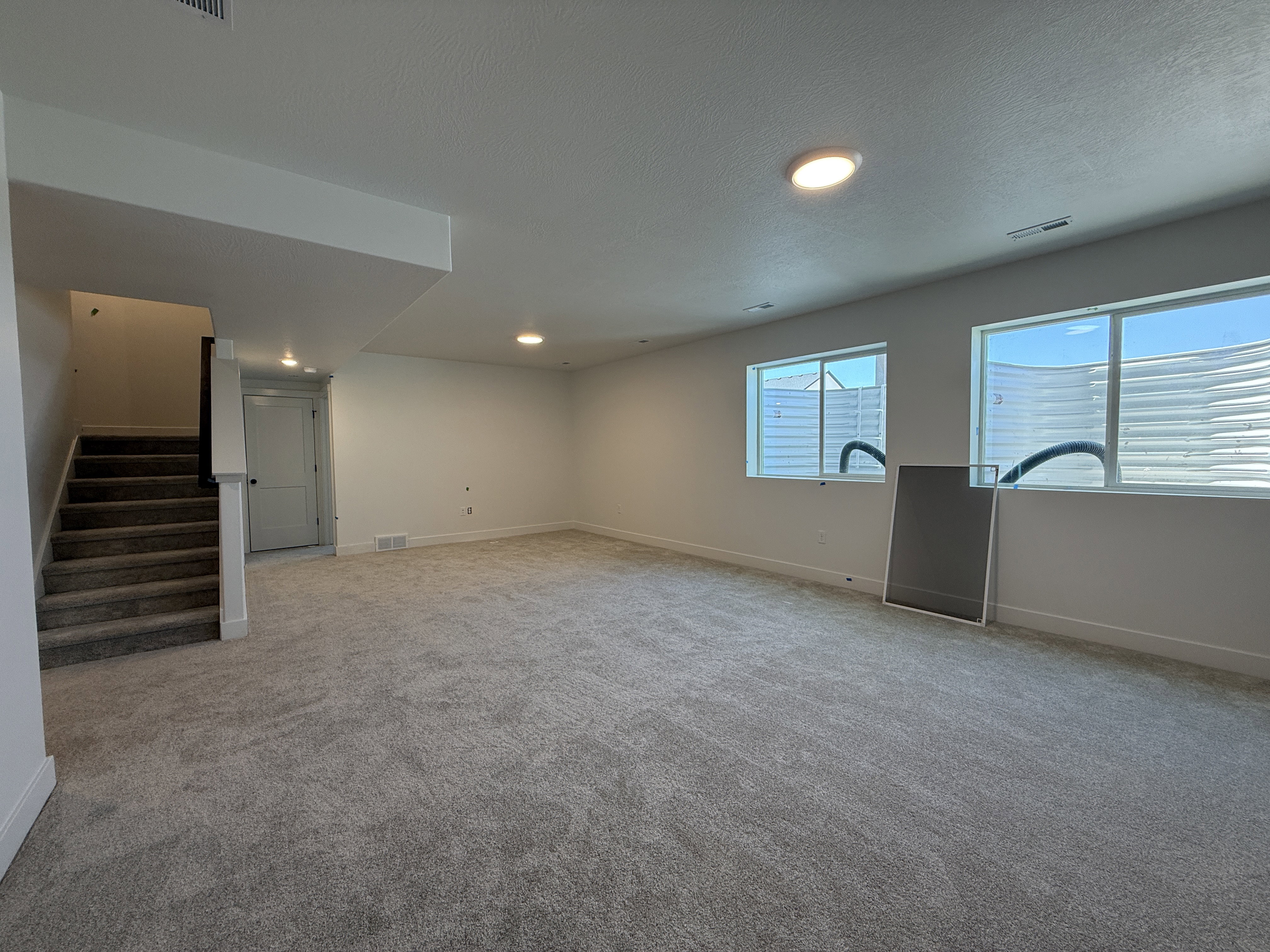 Spacious lower-level room featuring plush gray carpeting, recessed ceiling lighting, and two large egress windows