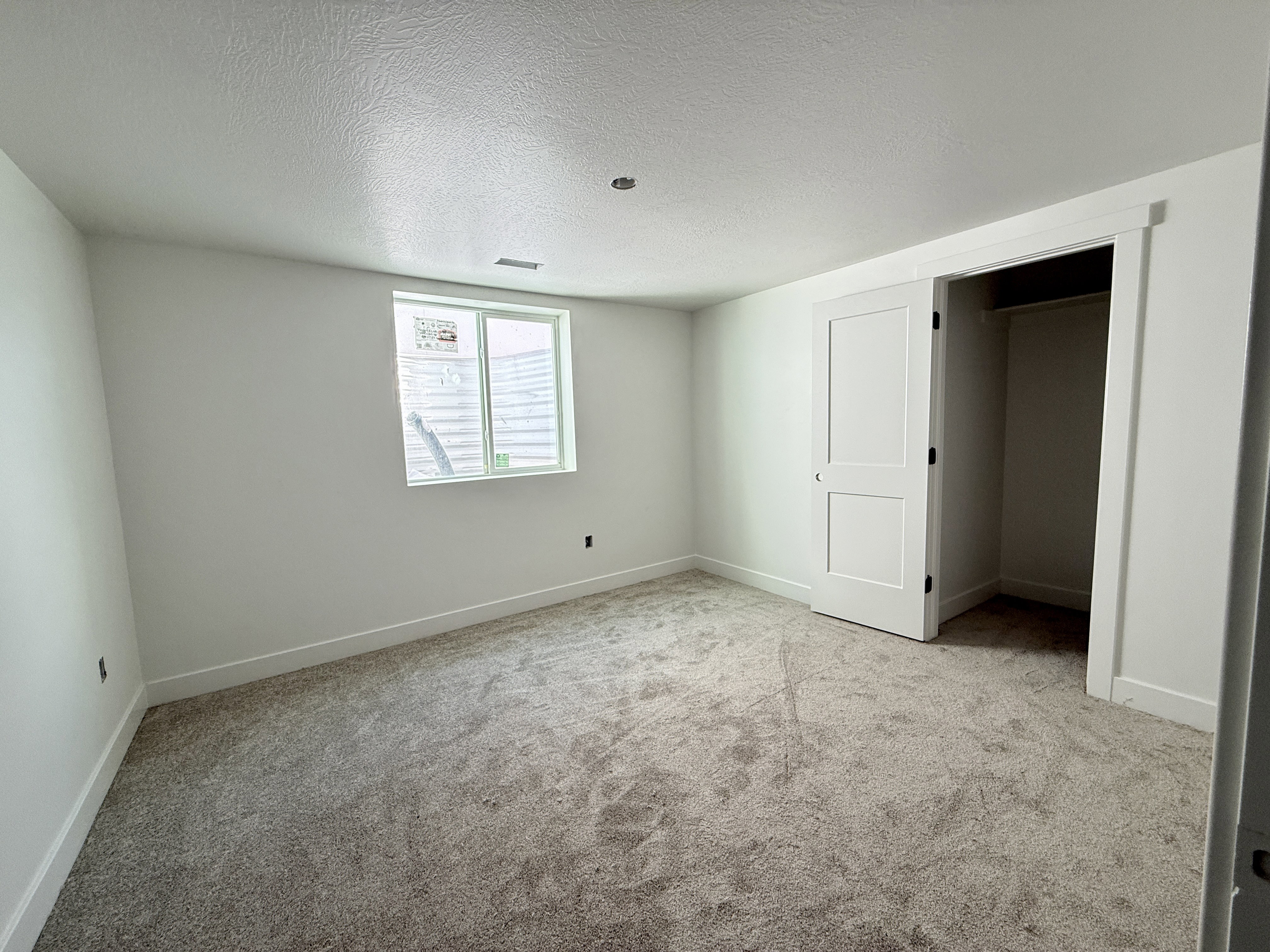 Bright room featuring a window with a horizontal blind, gray carpet, and white walls