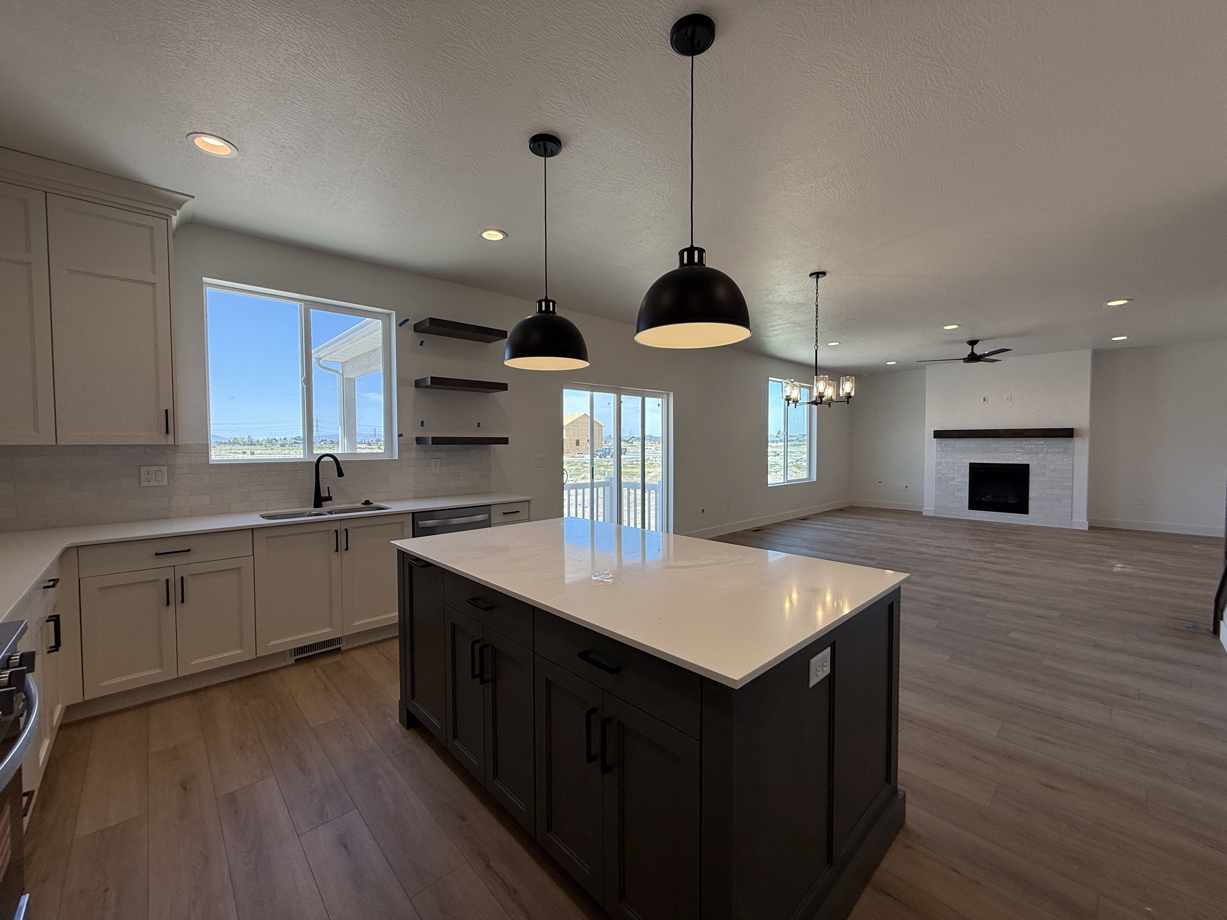 Open-concept living area featuring a kitchen island with a light-toned countertop, wood-finish flooring, and a fireplace with a tile surround and wood mantel