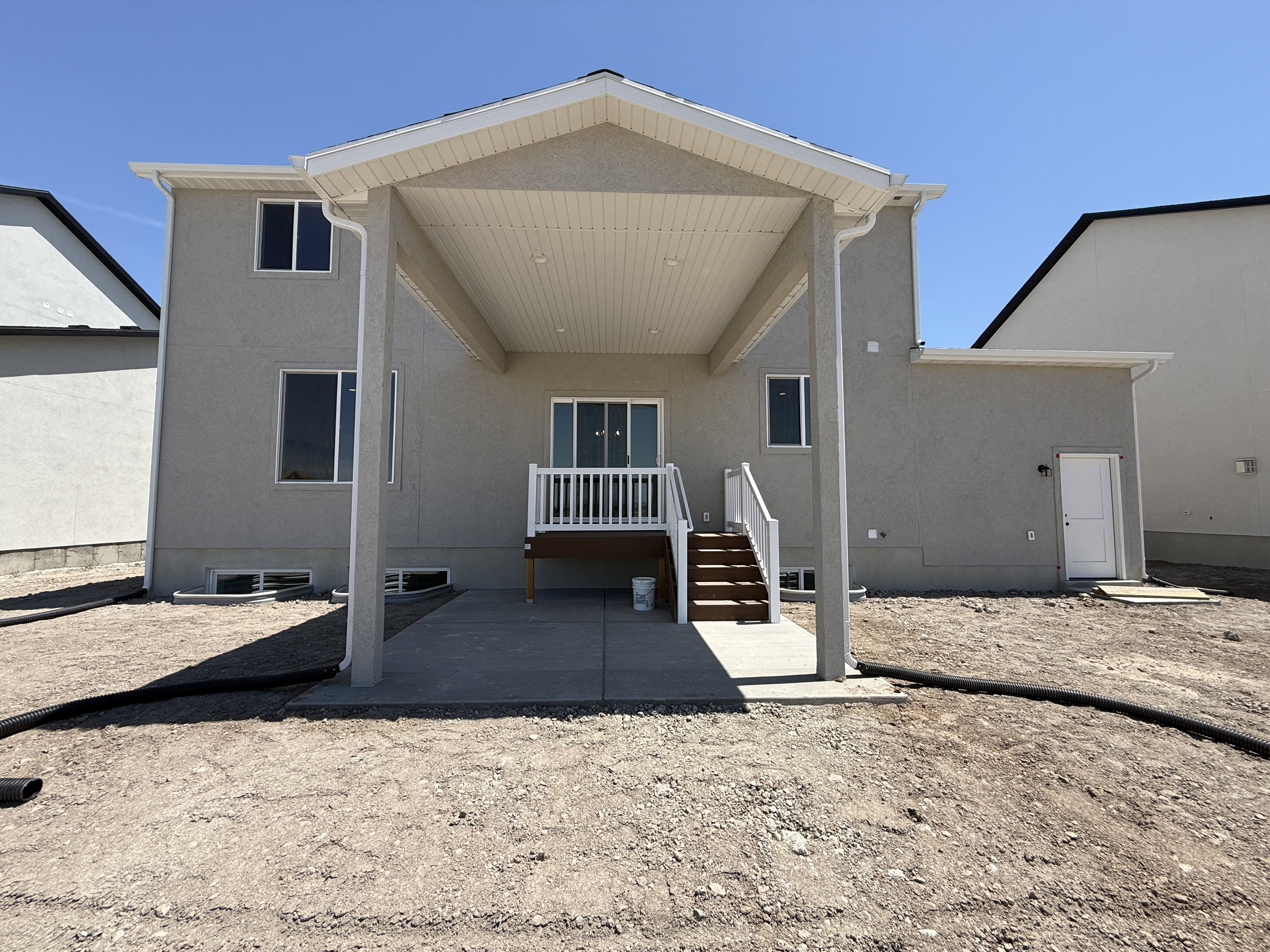 Rear elevation featuring a covered patio, concrete slab, and a wood deck with white railings
