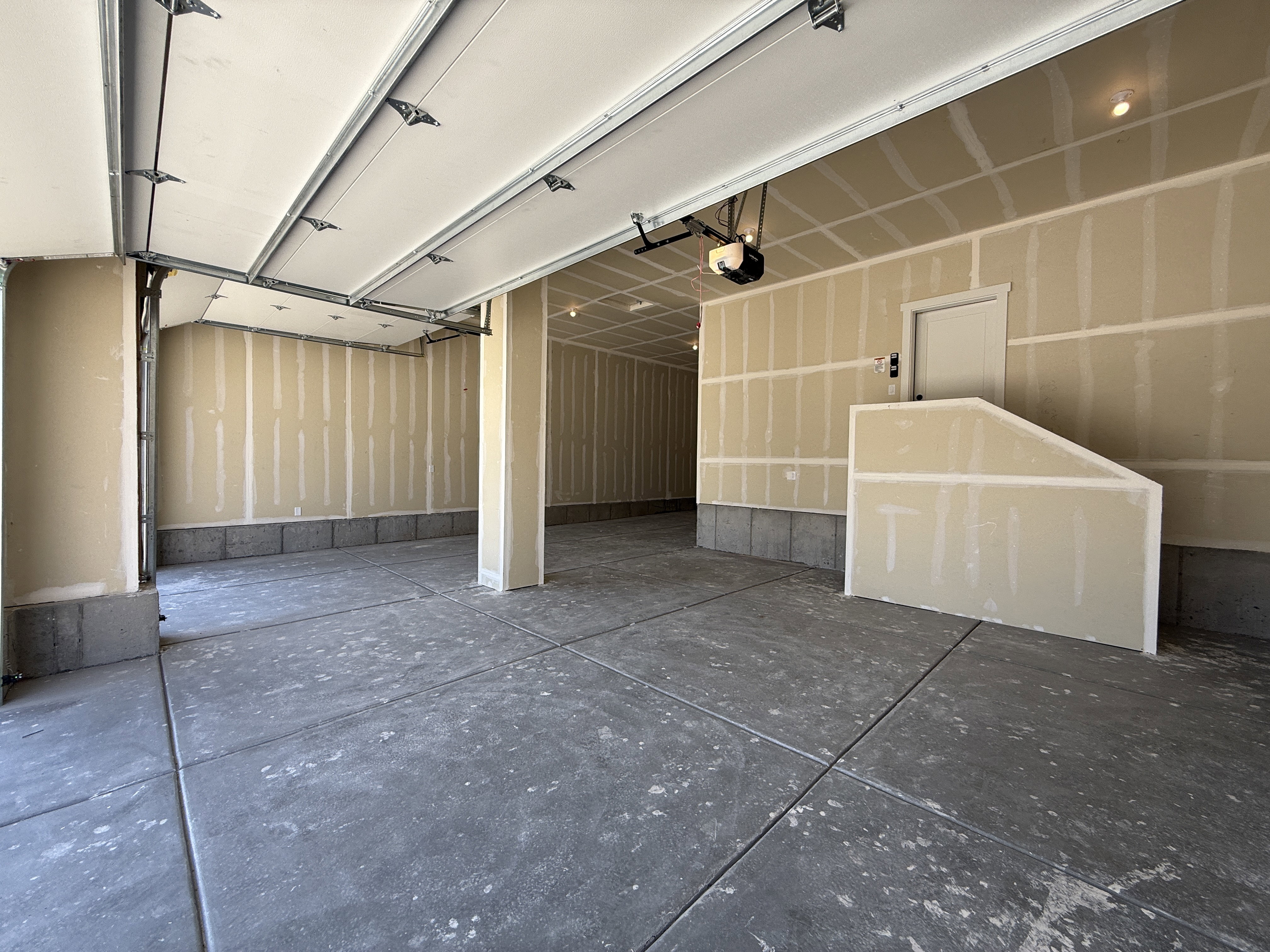 Spacious garage featuring a sectional overhead door with an automatic opener, concrete flooring, and unfinished drywall walls ready for customization