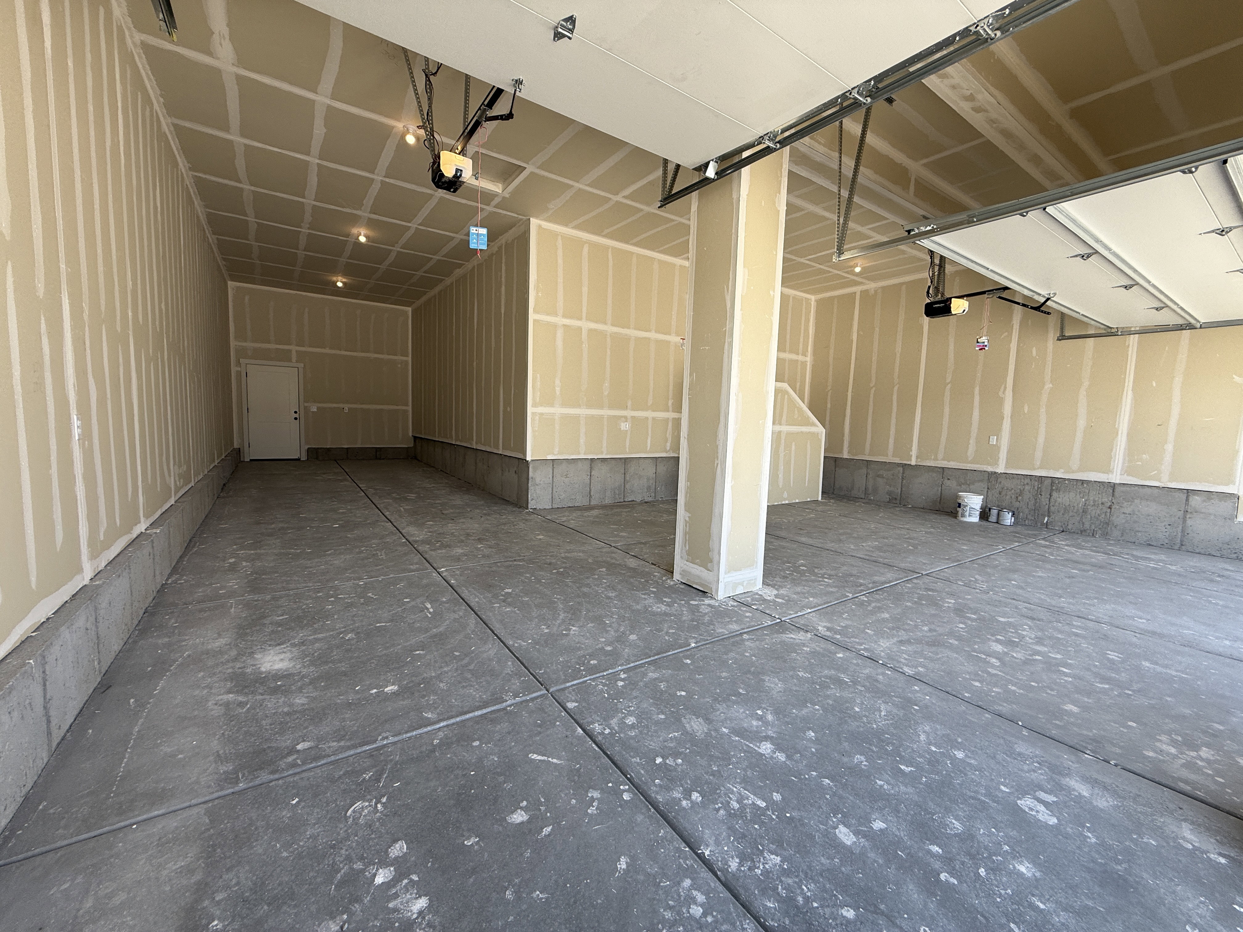 Spacious three-car garage featuring a concrete floor, exposed drywall walls, and overhead lighting