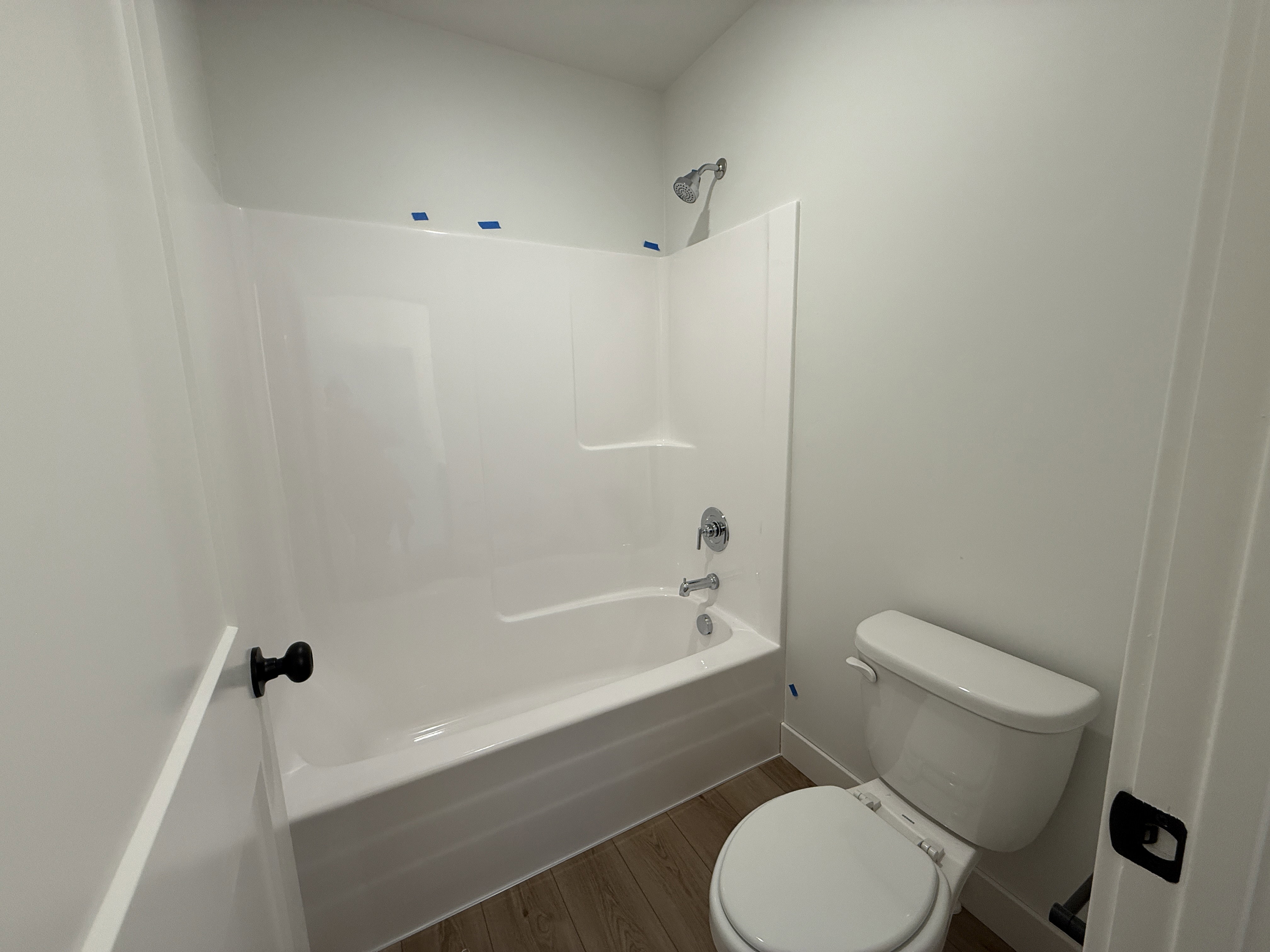 Bathroom featuring a white tub-shower combination with chrome fixtures, a white toilet, and wood-finish flooring