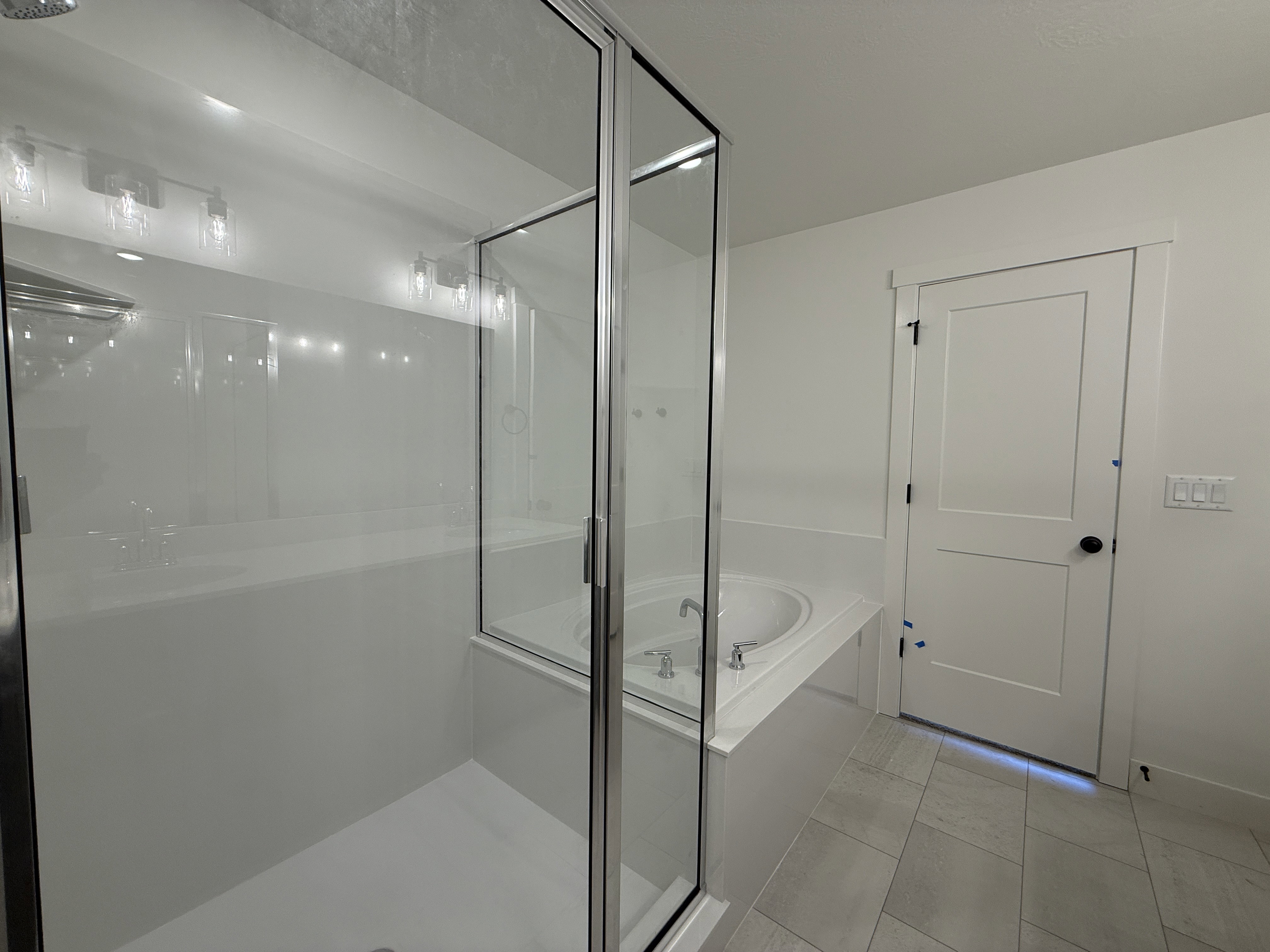 Glass-enclosed shower with a built-in tub, white panel door, and light-toned floor tiling