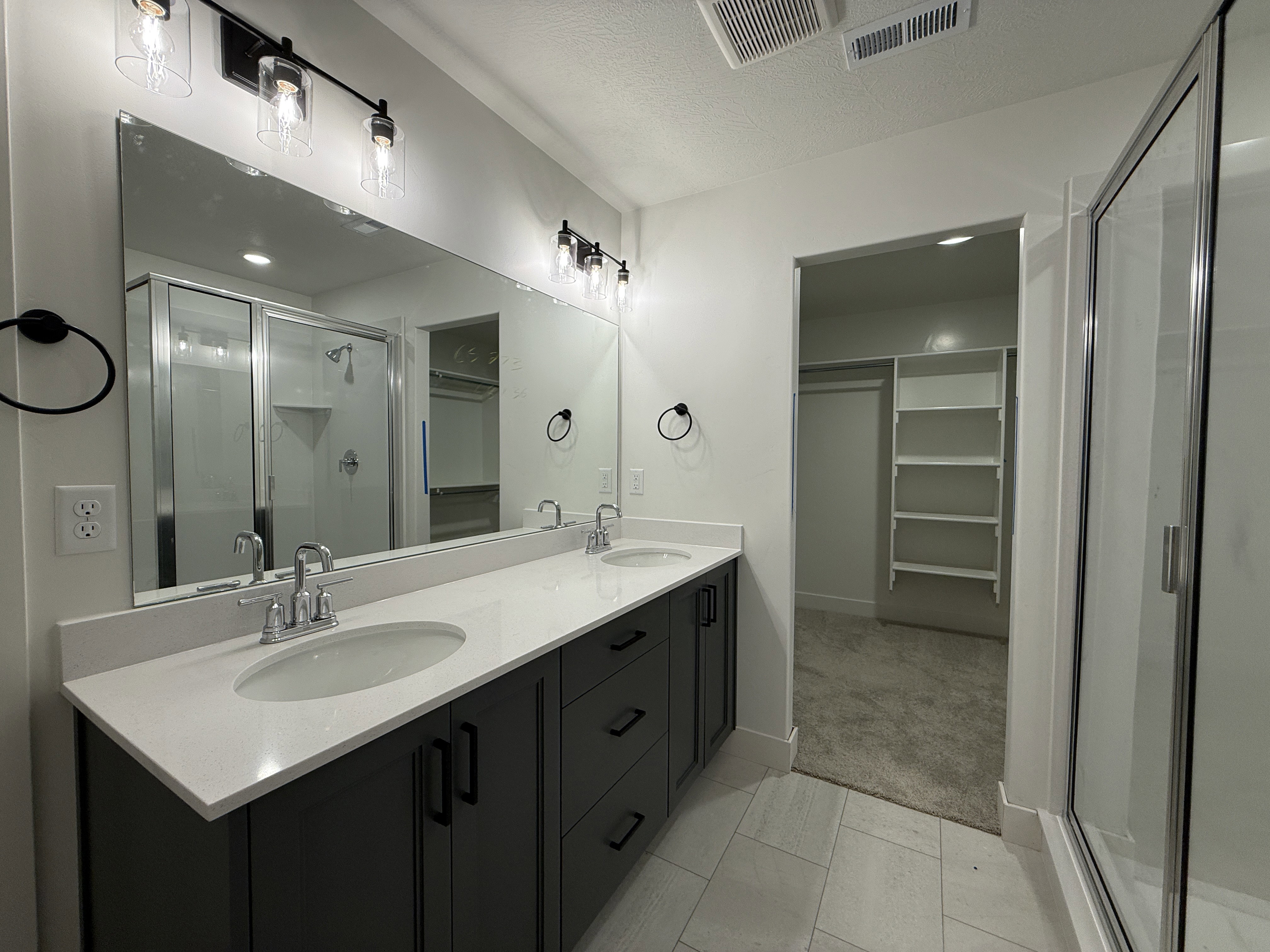 Dual vanity with a white countertop and dark cabinetry, featuring chrome fixtures and clear glass light sconces