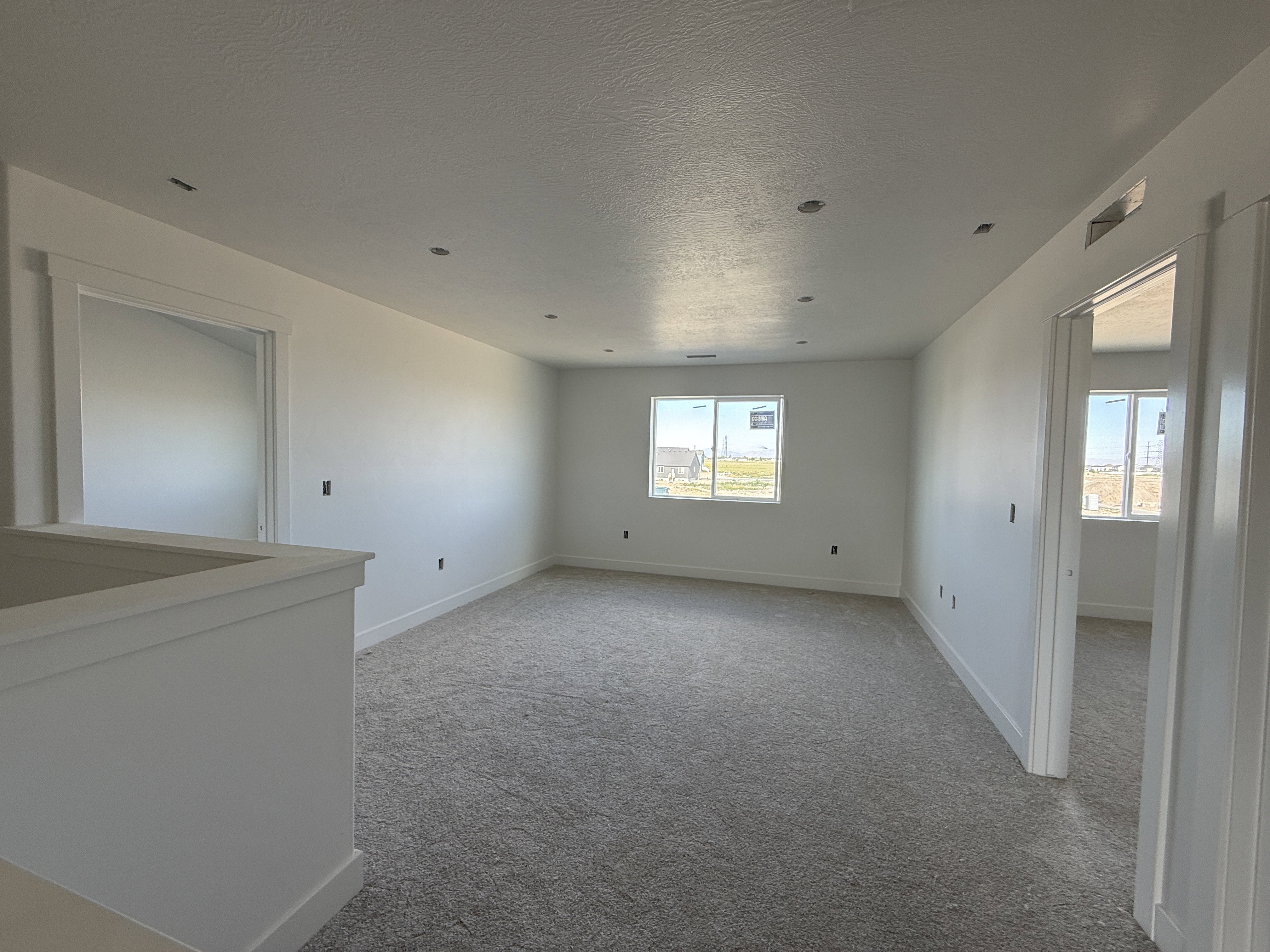 Open loft space featuring light gray carpet flooring, recessed ceiling lighting, and multiple windows