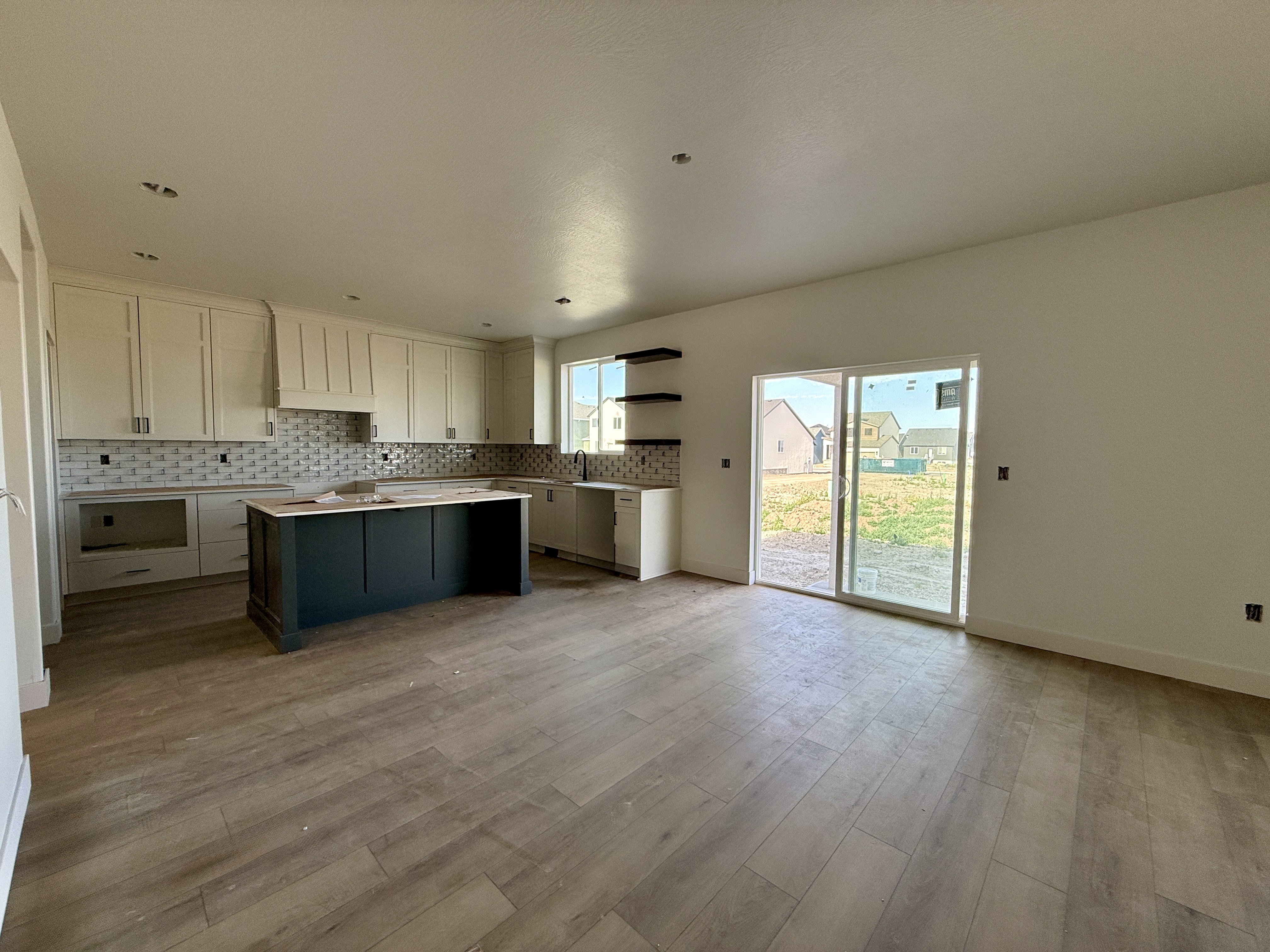 Spacious kitchen and dining area featuring light-toned shaker cabinetry, a dark-toned central island, and a geometric tile backsplash