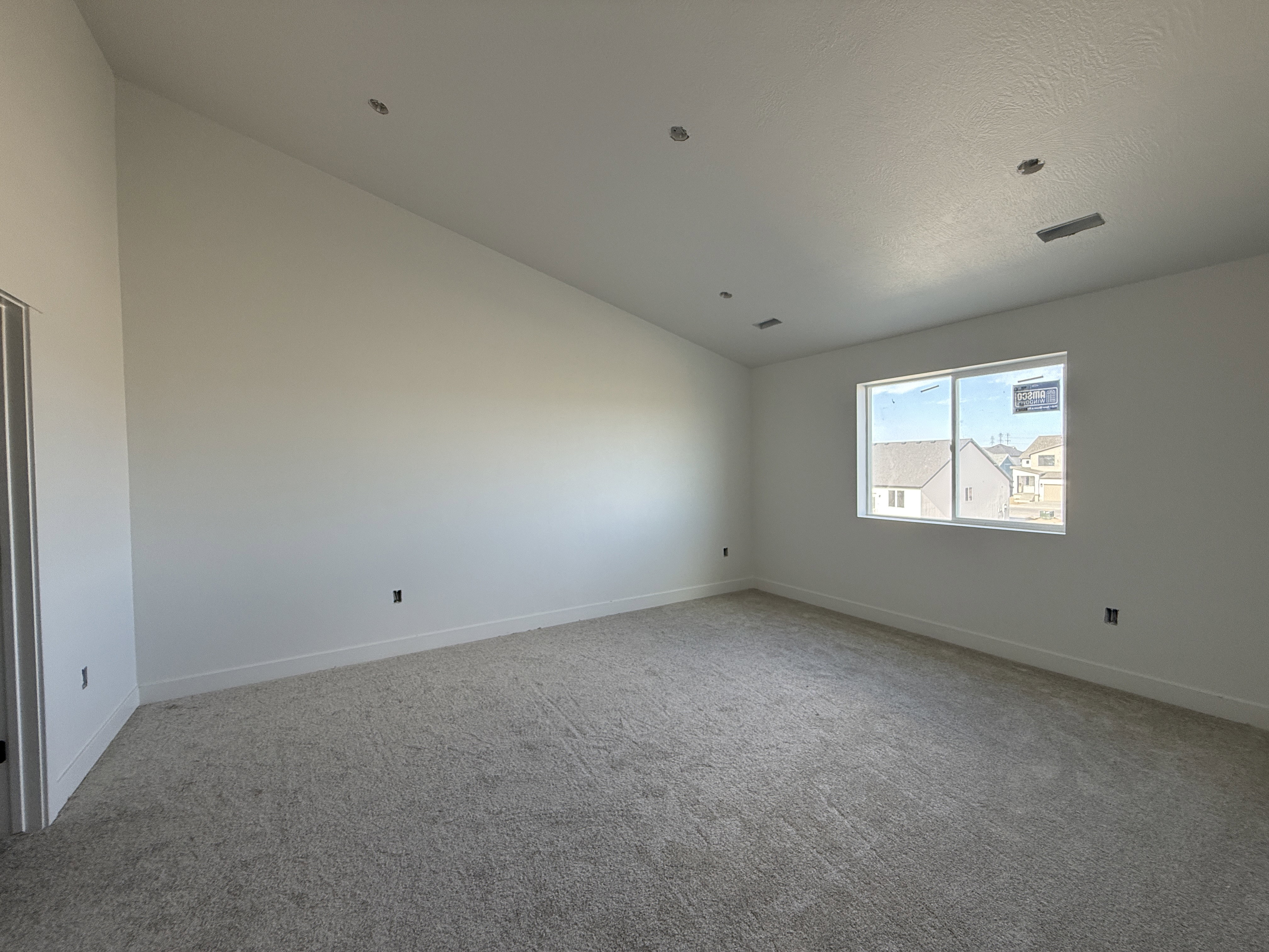 Spacious room featuring vaulted ceilings, light gray carpeting, and a large window providing ample natural light